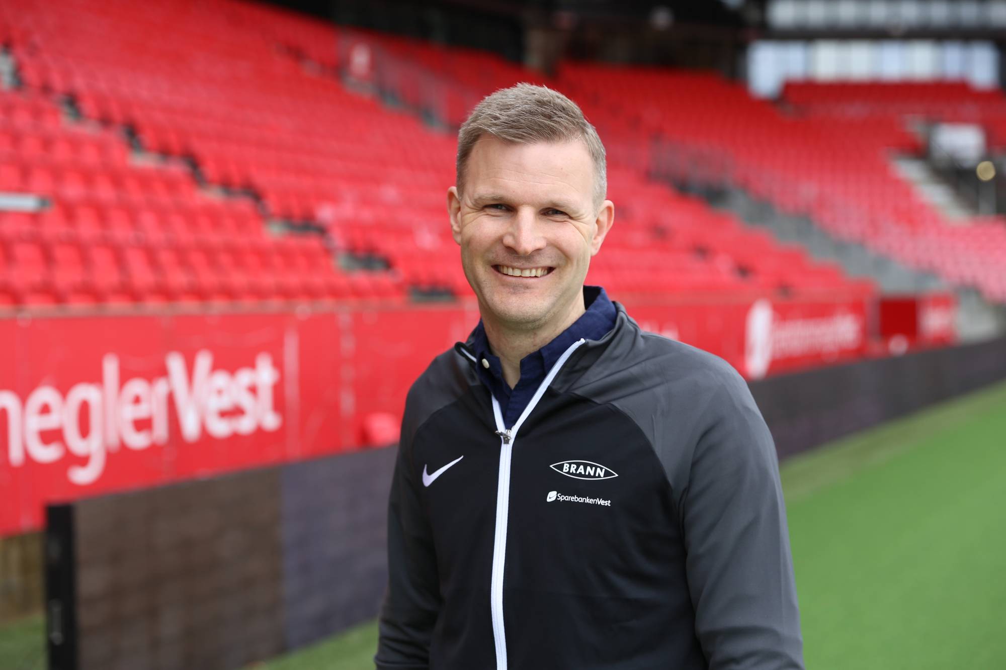 Christian Kalvenes, smiler foran rød tribune