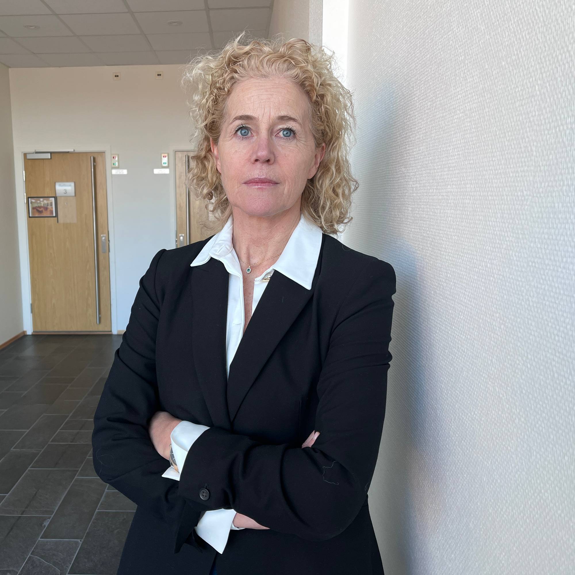 En kvinne med langt, lyst hår. Hun har på seg en hvit bluse og en mørk jakke.