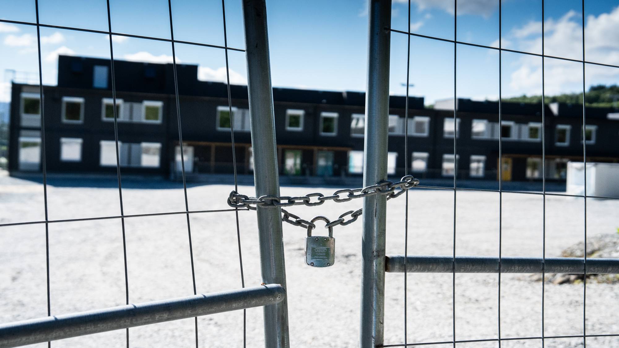 Bilde av skole med gjerde foran. Gjerdet er stengte med hengelås.