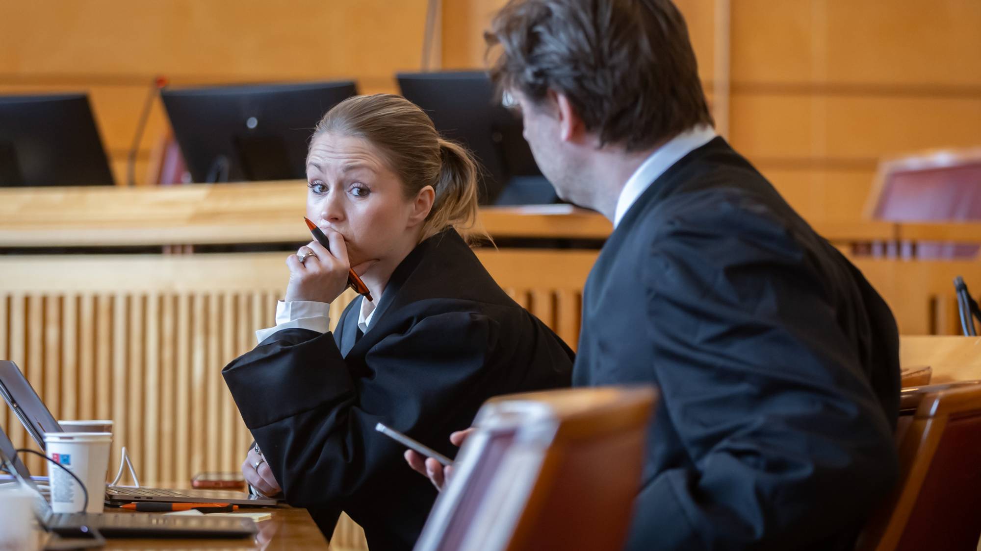 Forsvarerne Linn Haug Holm og Eirik Svingen Bjørgo. De sitter i en rettssal. Holm kikker noe betenkt i retning Bjørgo. Hun holder hånden til ansiktet og har en kulepenn i hendene. Vi ser Bjørgo fra siden.