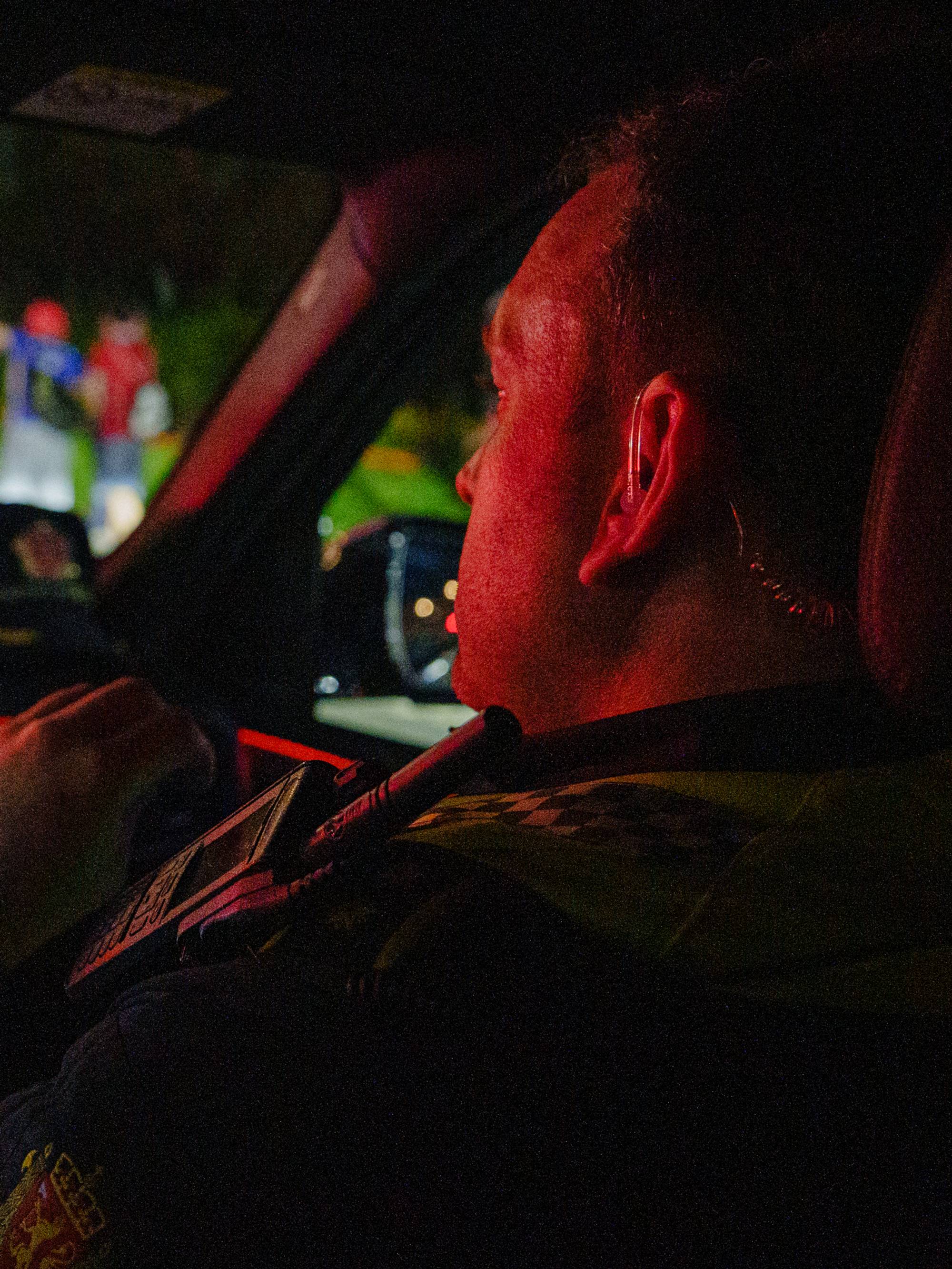 Politibetjent sitter i patruljebil og observerer personer på fortauet ved en vei om kvelden. 