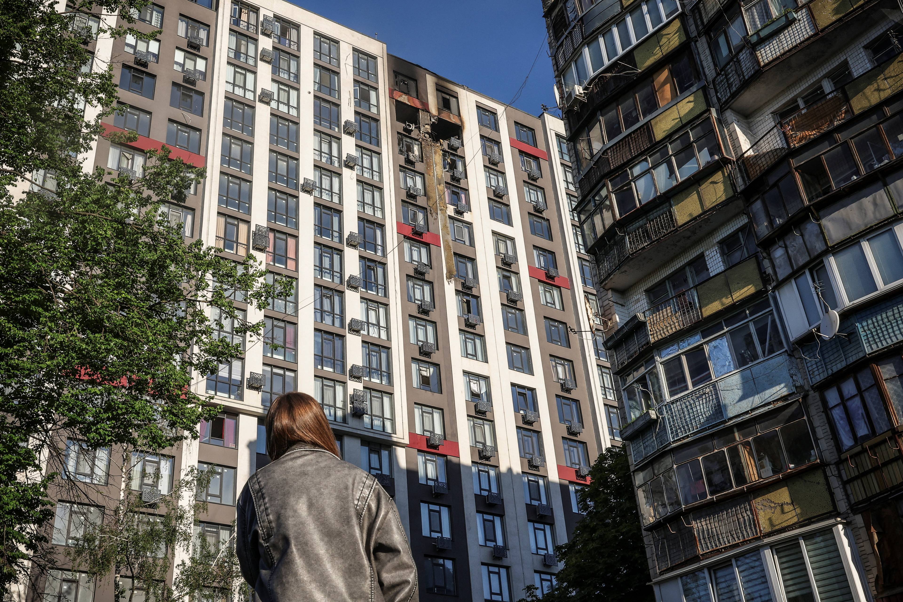 Kvinne i skinnjakke ser på en høyblokk der toppen er svart og brent