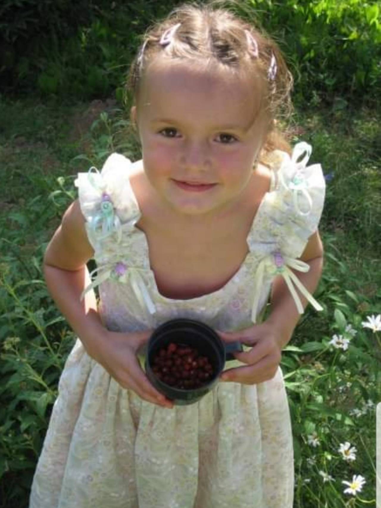 Andrine som barn står i en hage med blomstrete lys kjole og har plukket bær i en kopp.