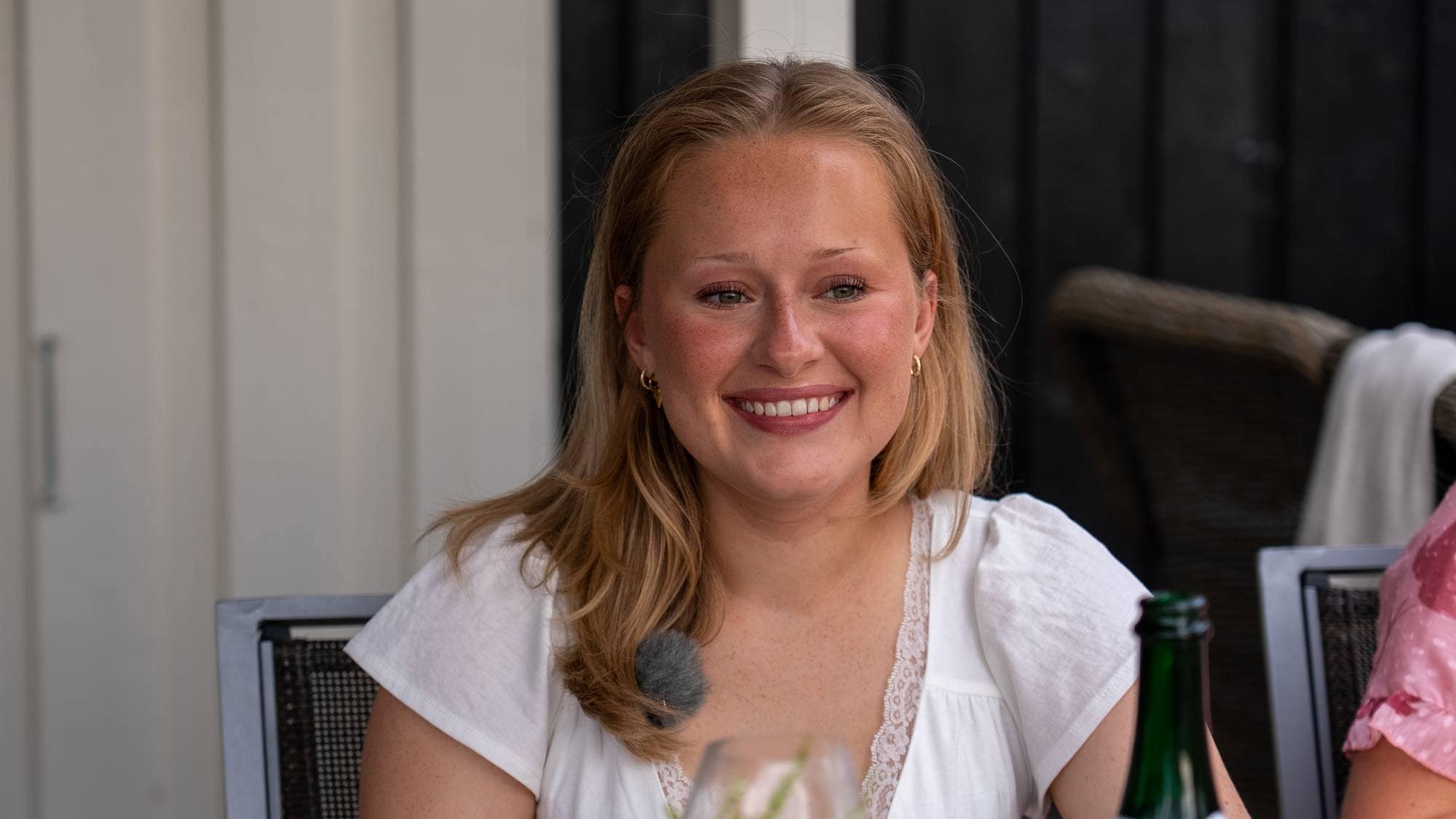 En smilende kvinne sitter ved et bord med en drink. (Bildebeskrivelsen er laget av en KI-tjeneste)