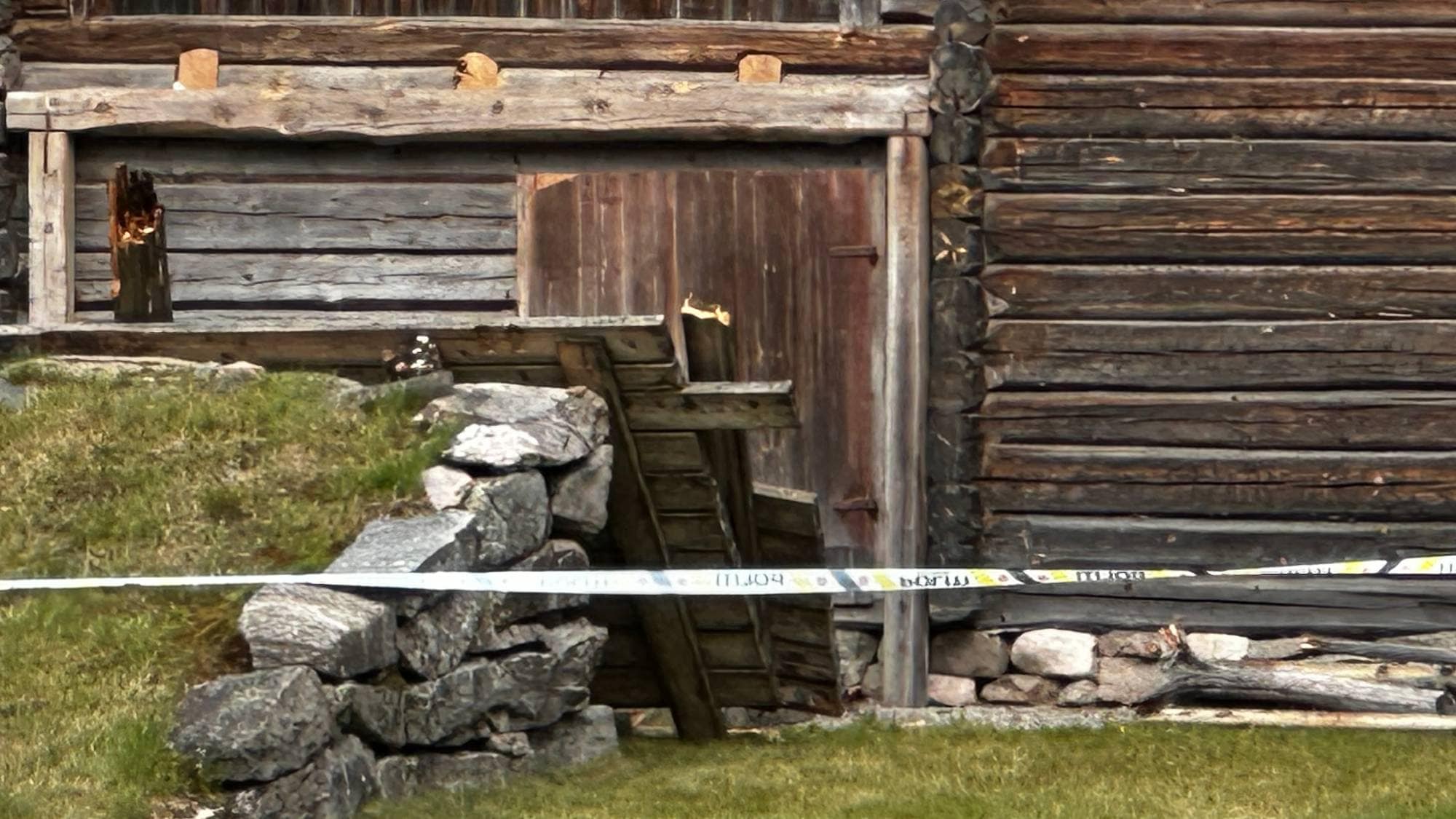 Politistrimmel sperrer av et område ved en tømmerbygning og en steinmur.