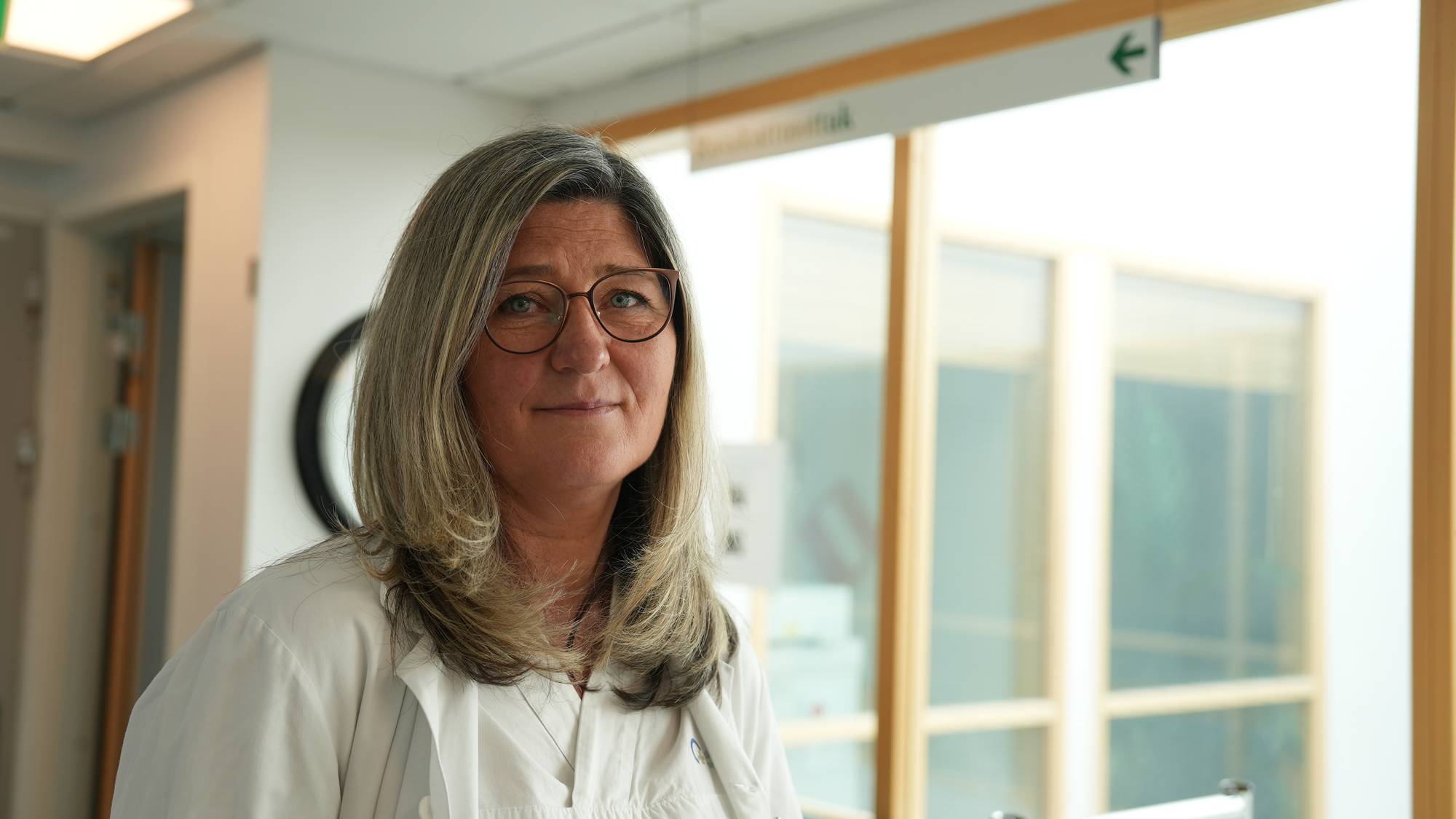 Jelena Staalstrøm har på seg legeuniform og briller og ser inn i kameraet. Hun står i korridoren på rusakuttmottaket i Oslo 