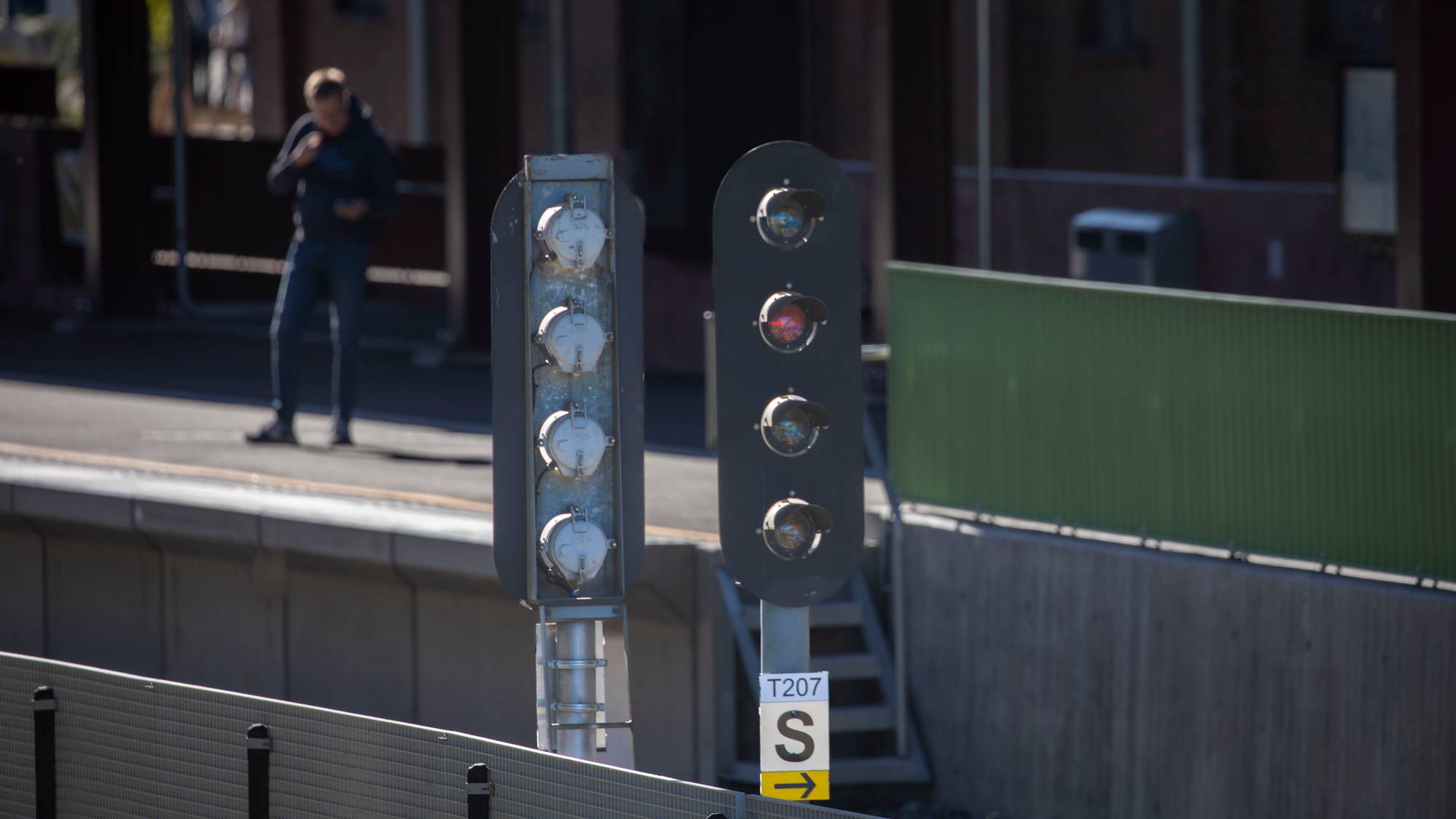 Et rødt lyssignal ved en togperrong. En person står i bakgrunnen. (Bildebeskrivelsen er laget av en KI-tjeneste)