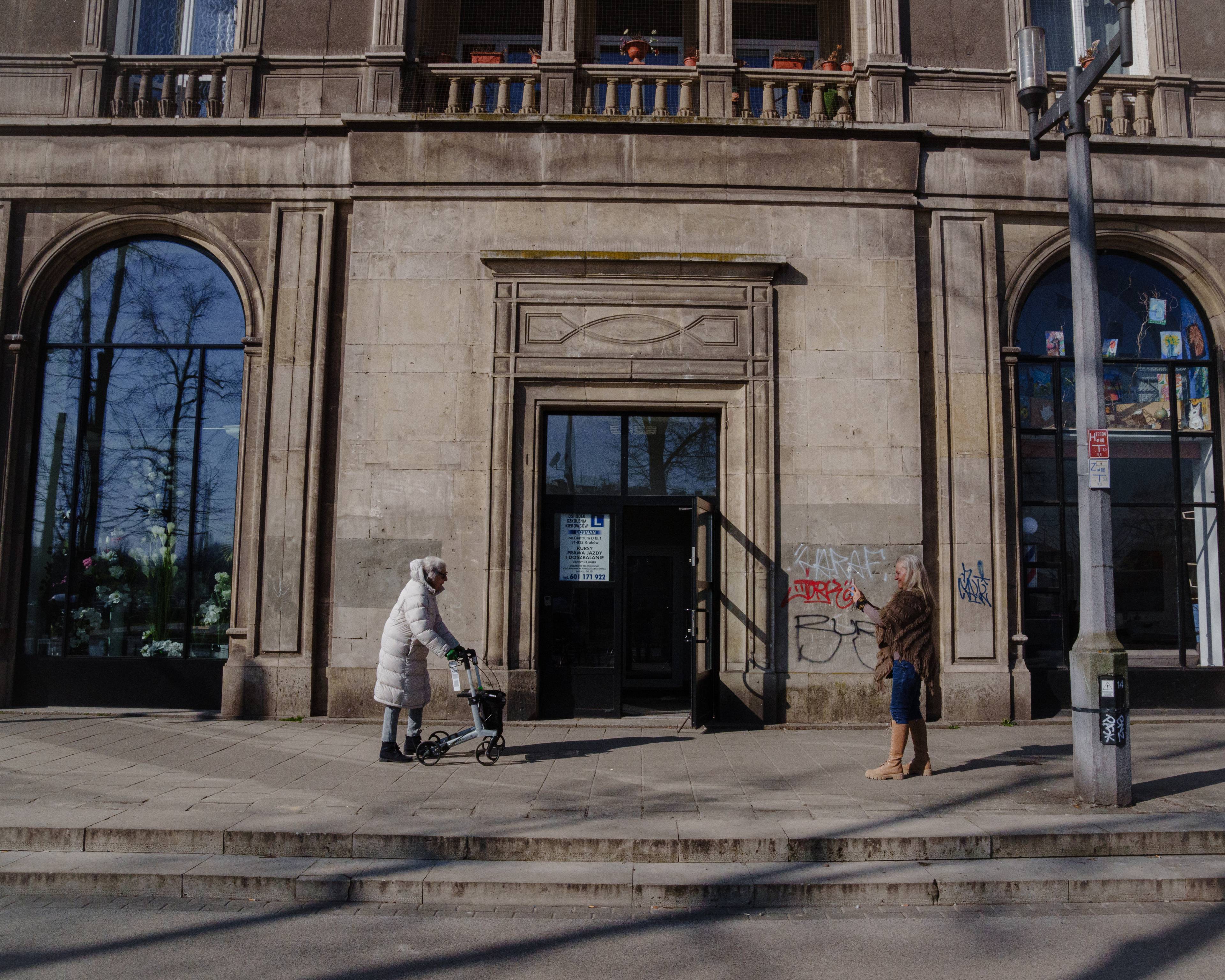 Magdalena og Edith går et stykke fra hverandre på en solfylt gate foran en stor bygning
