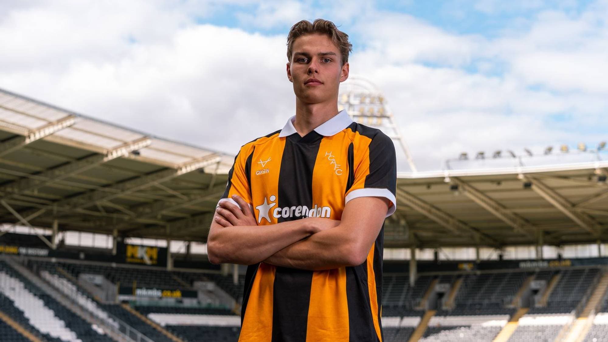 Fotballspiller i Hull City-drakt står med armene i kors på en fotballstadion. (Bildebeskrivelsen er laget av en KI-tjeneste)