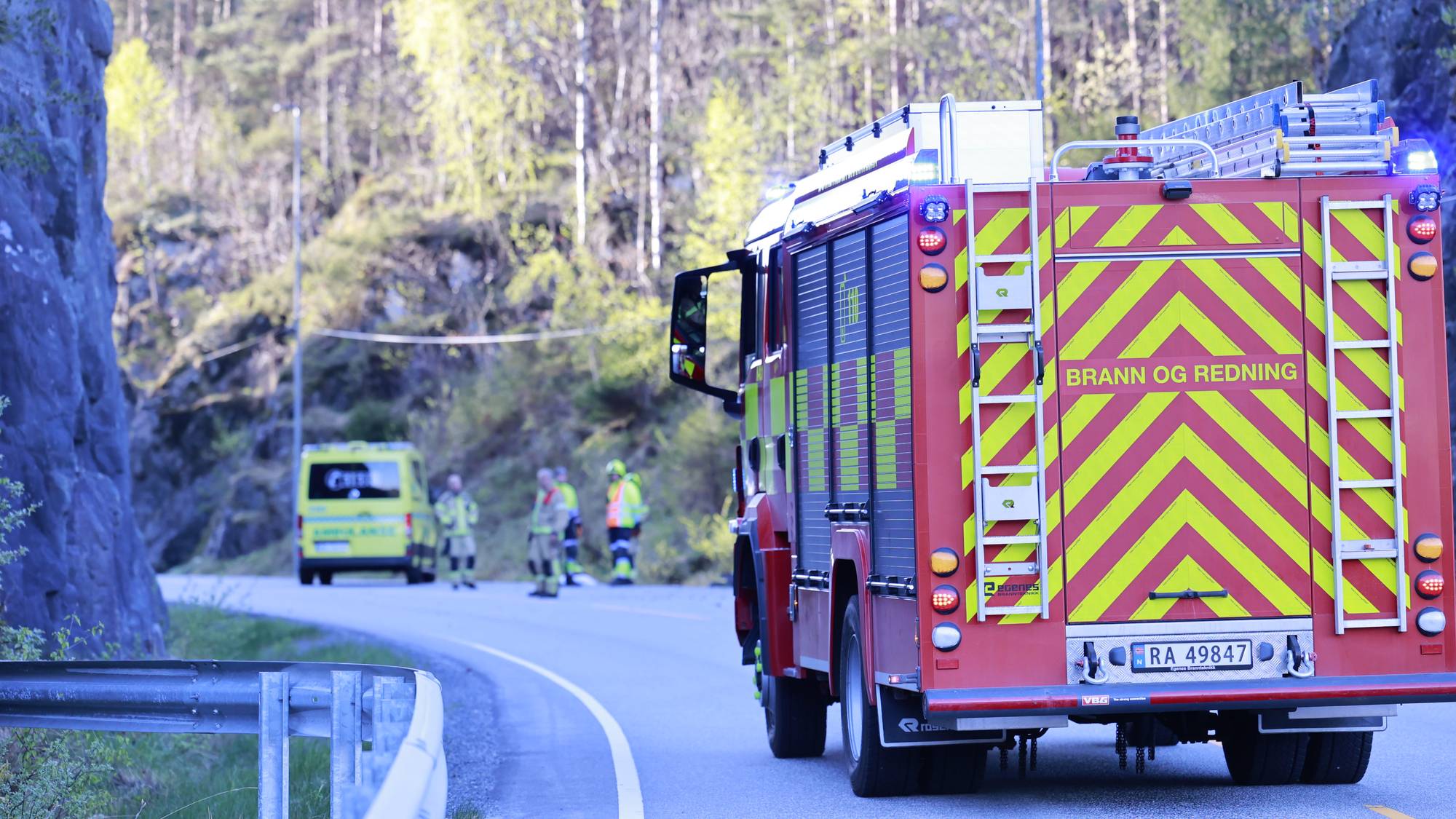 En brannbil står i forgrunnen. I bakgrunnen ser man en ambulanse og flere brannmenn og ambulansefolk.