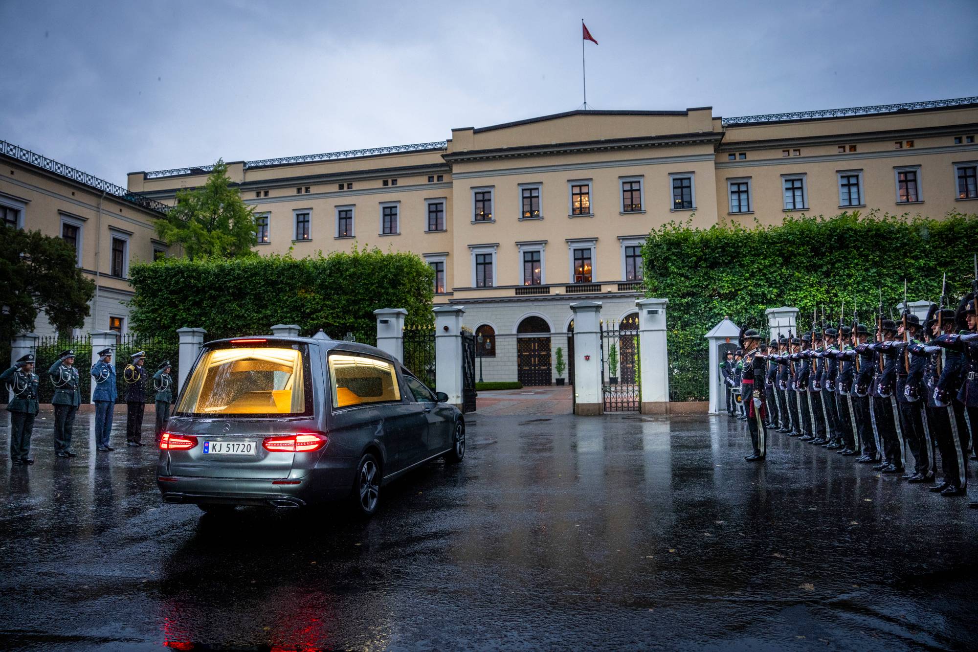 Bårebilen med kong Haralds kjører inn til Slottet, på den ene siden står Garden, og på den andre står kongens adjutanter og gjør honnør