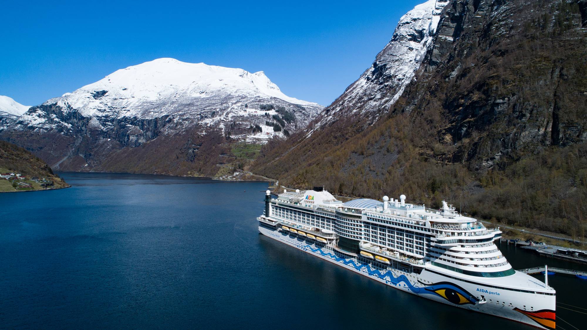 Cruiseskip i Geiranger. Snøen ligg framleis i fjella. Skipet AIDAPerla ligg innerst i fjorden.