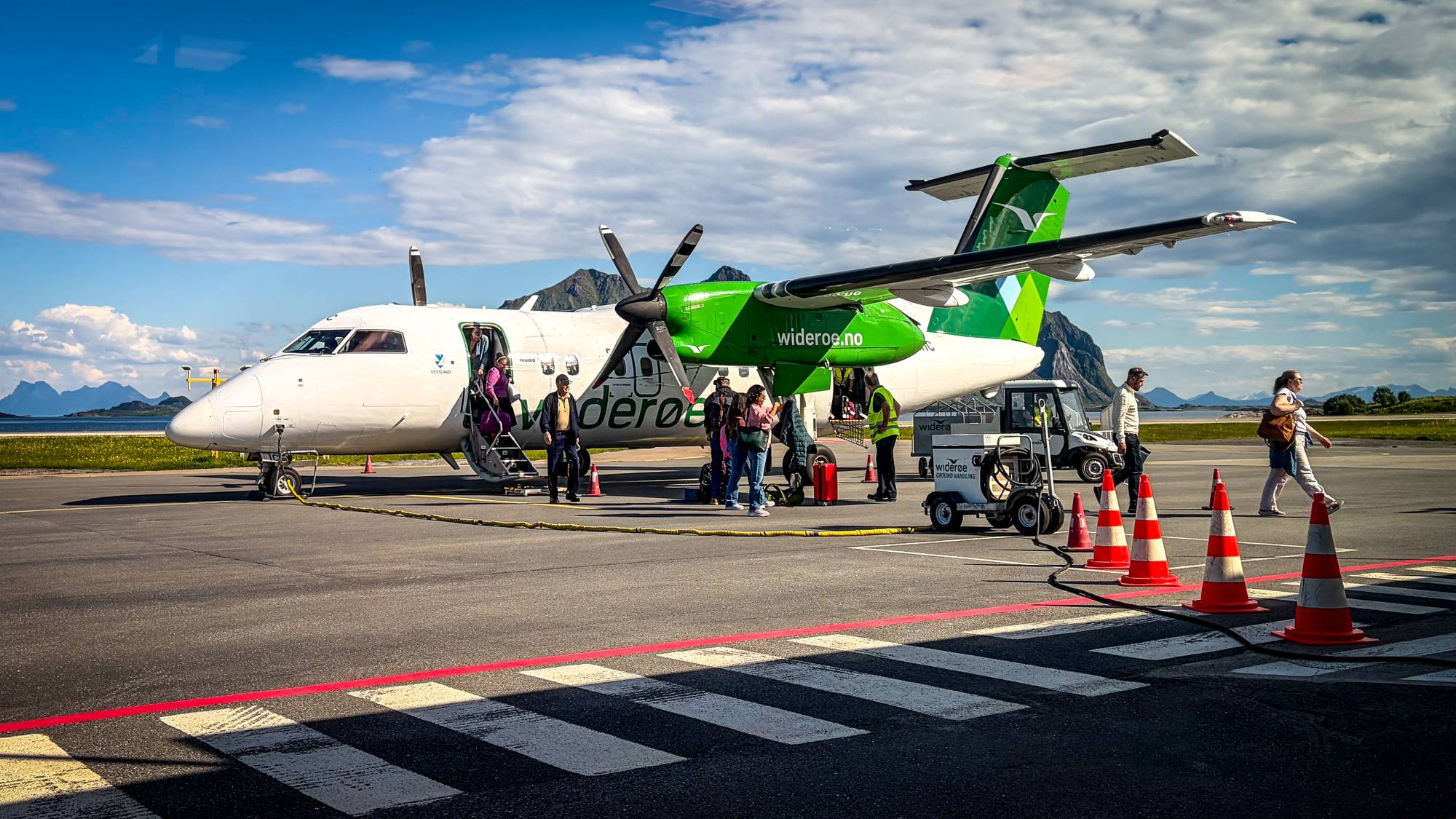 Folk på vei ut av et Widerøe-fly i solskinn