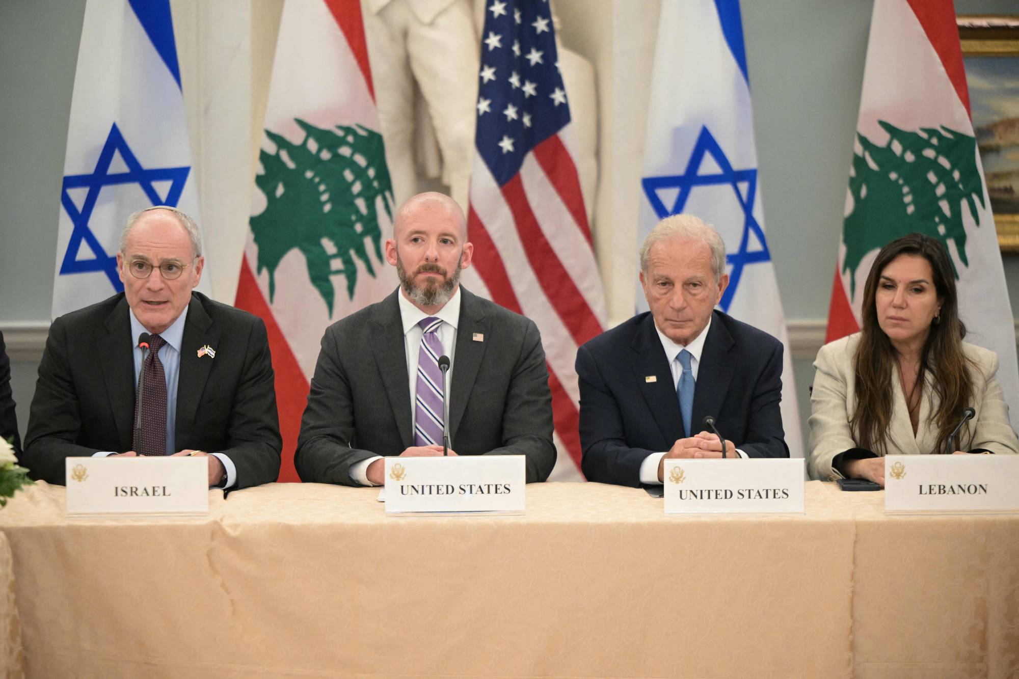 Fire personer sitter bak et bord med nasjonalflagg. Fra venstre: en mann med briller og dress, en mann med kort hår og dress, en eldre mann med dress og en kvinne med lys dress. Skilt på bordet viser "ISRAEL", "UNITED STATES" og "LEBANON". (Bildebeskrivelsen er laget av en KI-tjeneste)