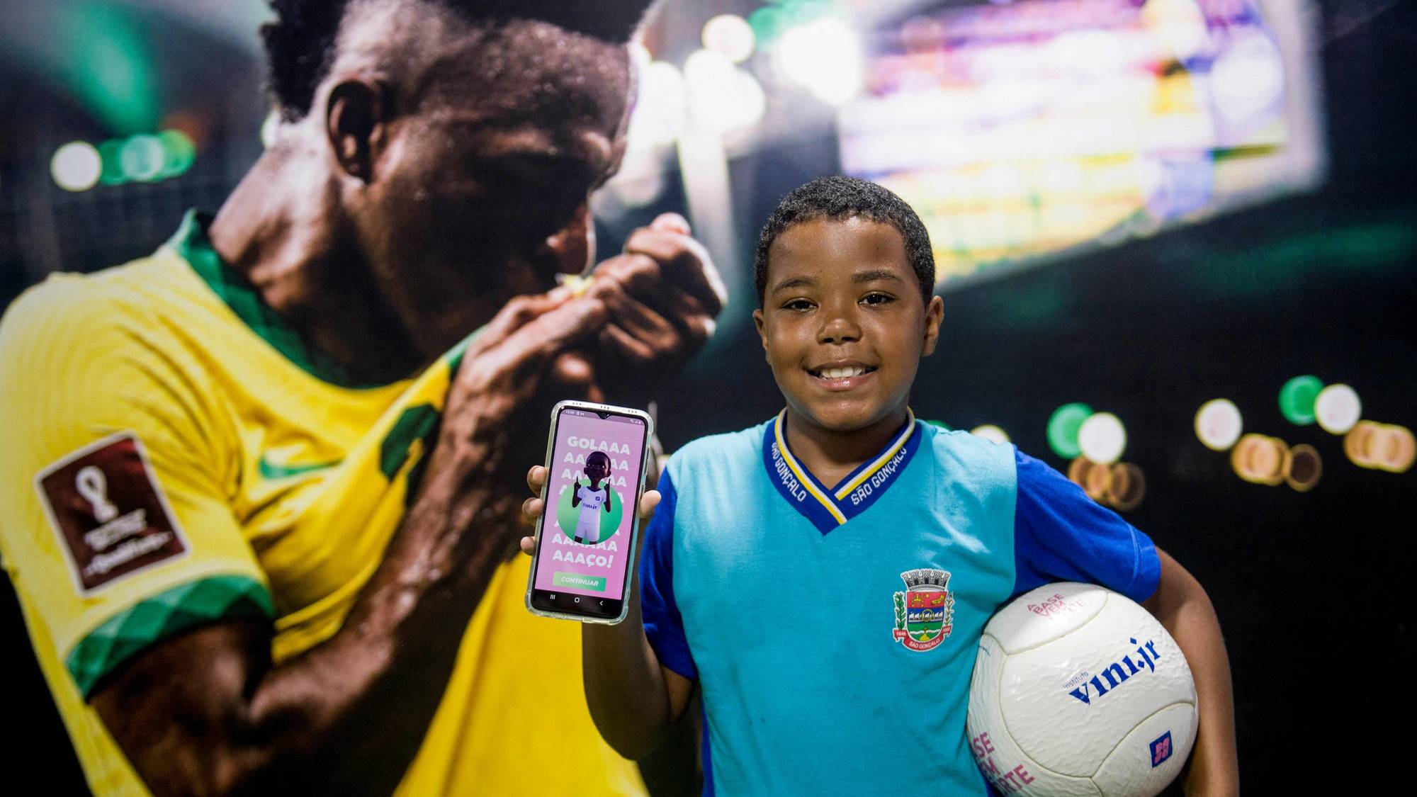 Gutt holder en smarttelefon med et bilde av Vinicius Junior, foran et stort bilde av fotballspilleren. (Bildebeskrivelsen er laget av en KI-tjeneste)
