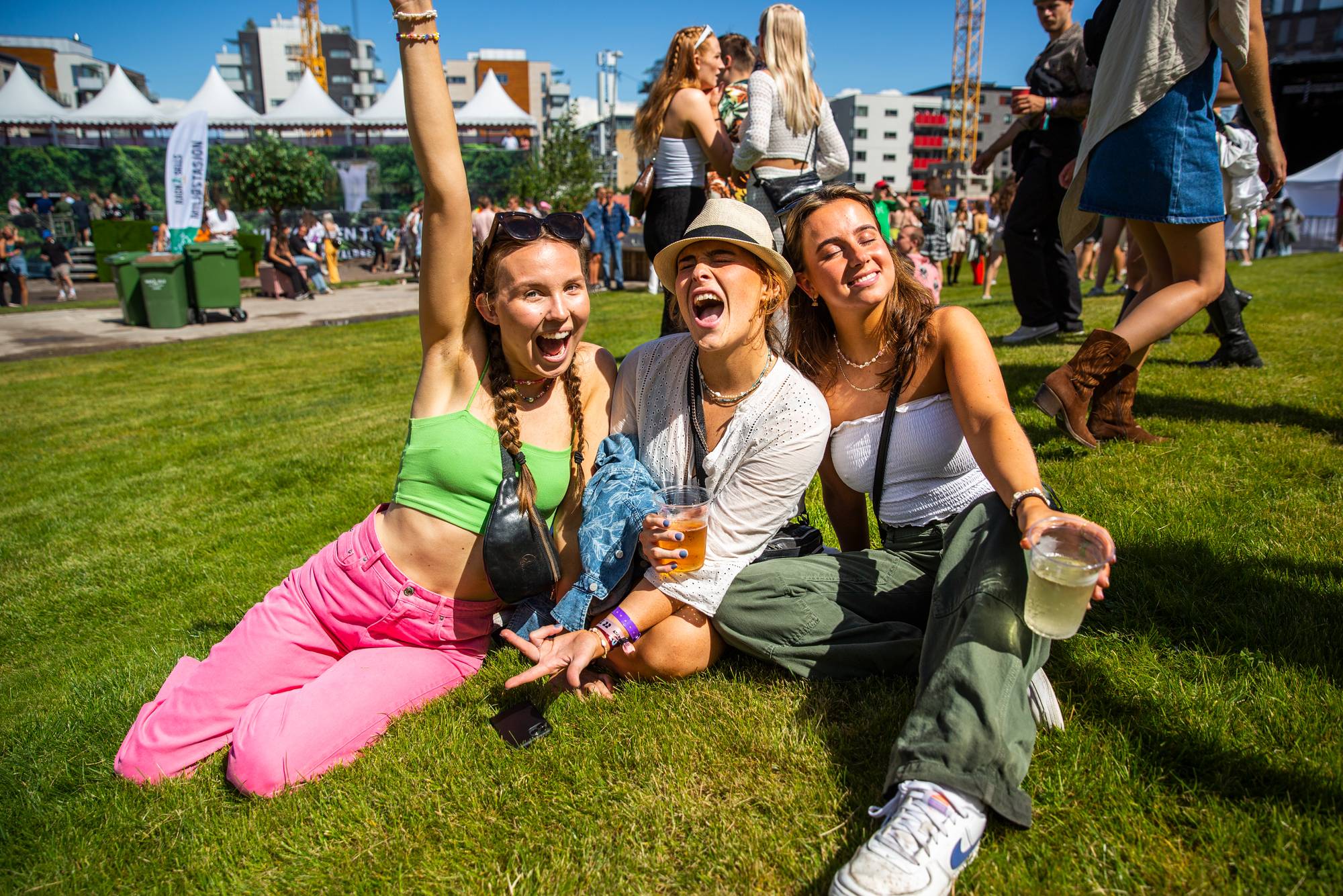 Tre jenter sitter på gresset på Slottsfjell og jubler. 