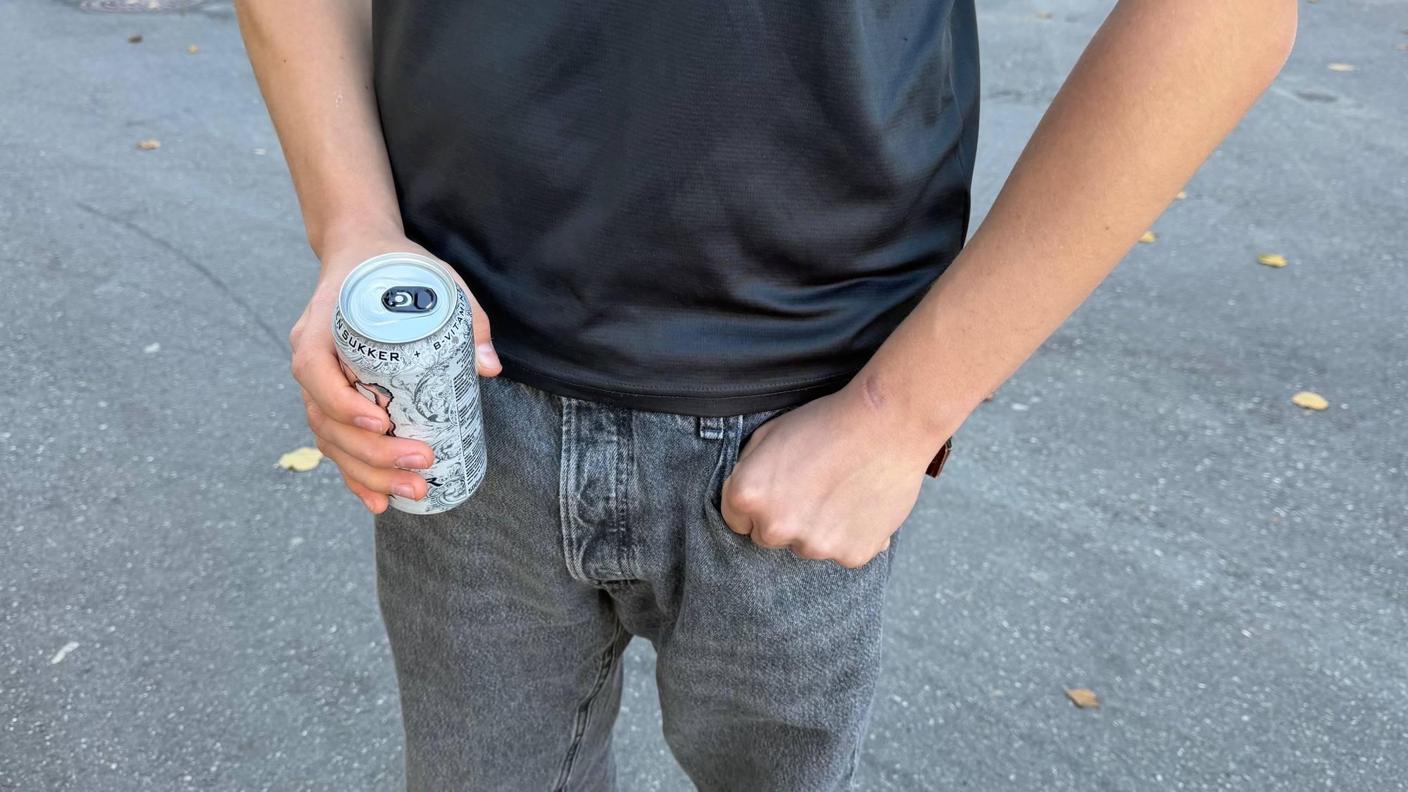 Underkroppen på anonym mannsperson som holder i brusboks i gatemiljø