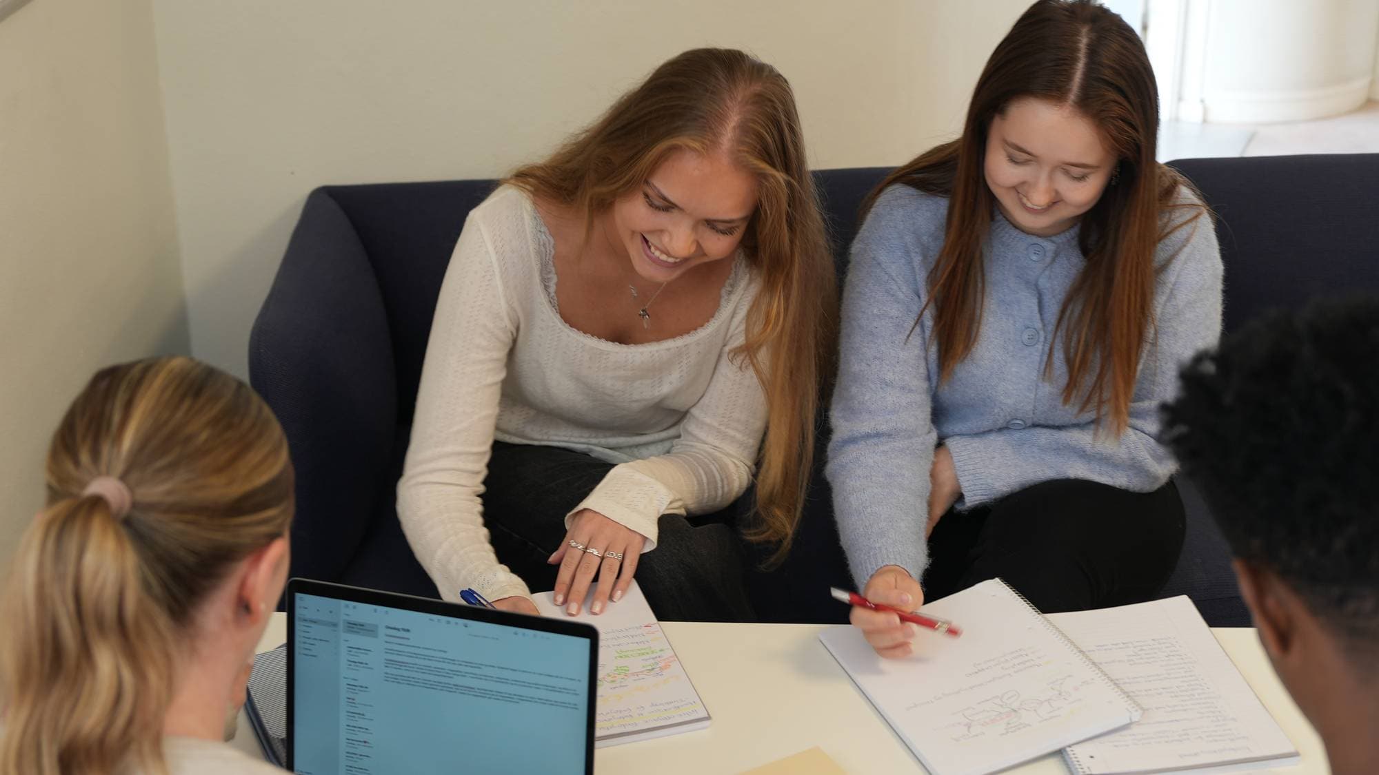 Elevene sitter i en gruppe rundt et bord og gjør skolearbeid. De har skrivebøker med seg, og holder en penn i hånden. 