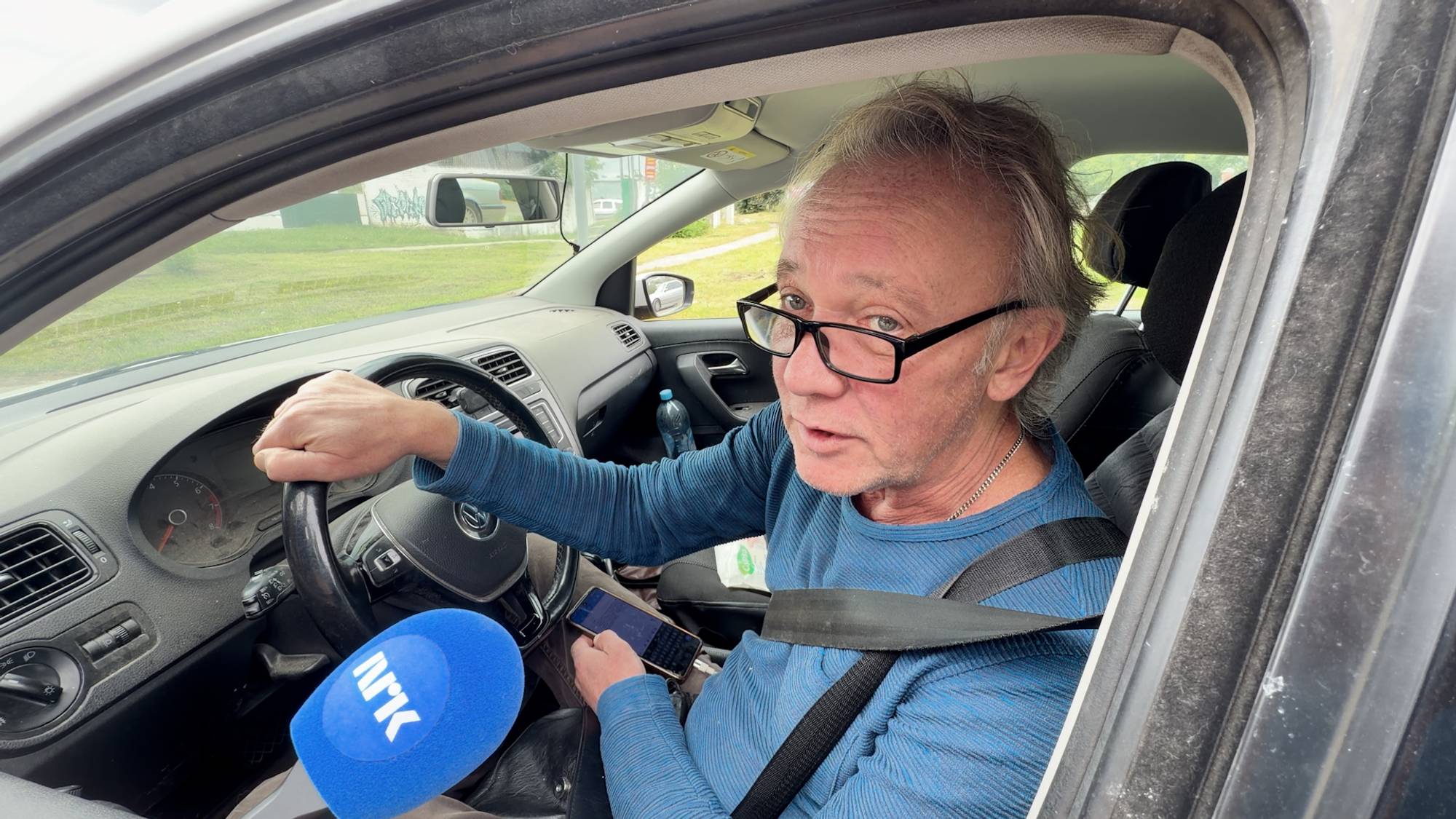 mann sitter i førerseter av en bil og blir intervjuet.