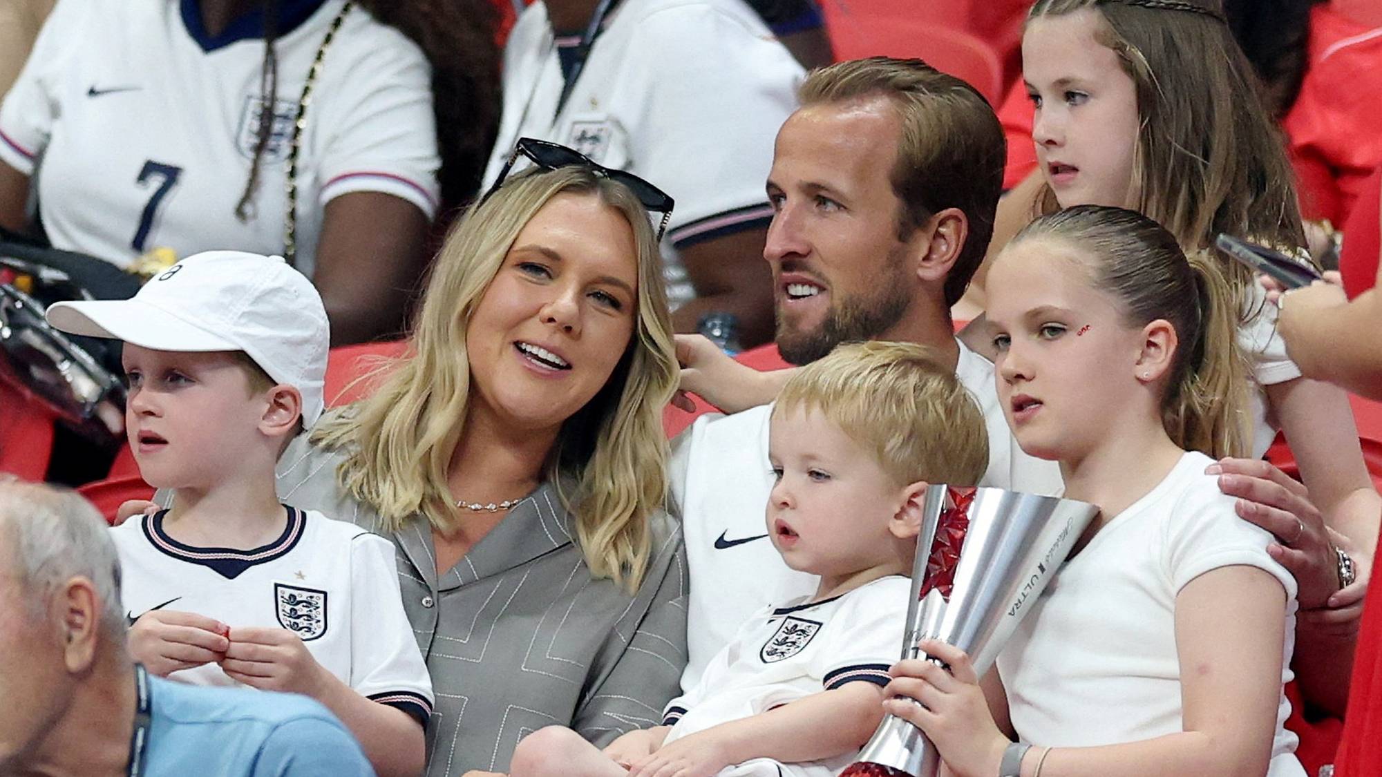 Fotballspiller Harry Kane sitter sammen med familien sin på tribunen under en kamp. (Bildebeskrivelsen er laget av en KI-tjeneste)