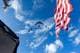 US Navy / Reuters / NTB Fly passerer over et område med en amerikansk flagg i forgrunnen. Værforholdene er klare med blå himmel og spredte skyer. Flagget vaier i vinden, mens jetflyene er synlige i høyden. Omgivelsene antyder en utendørs feiring eller arrangement.