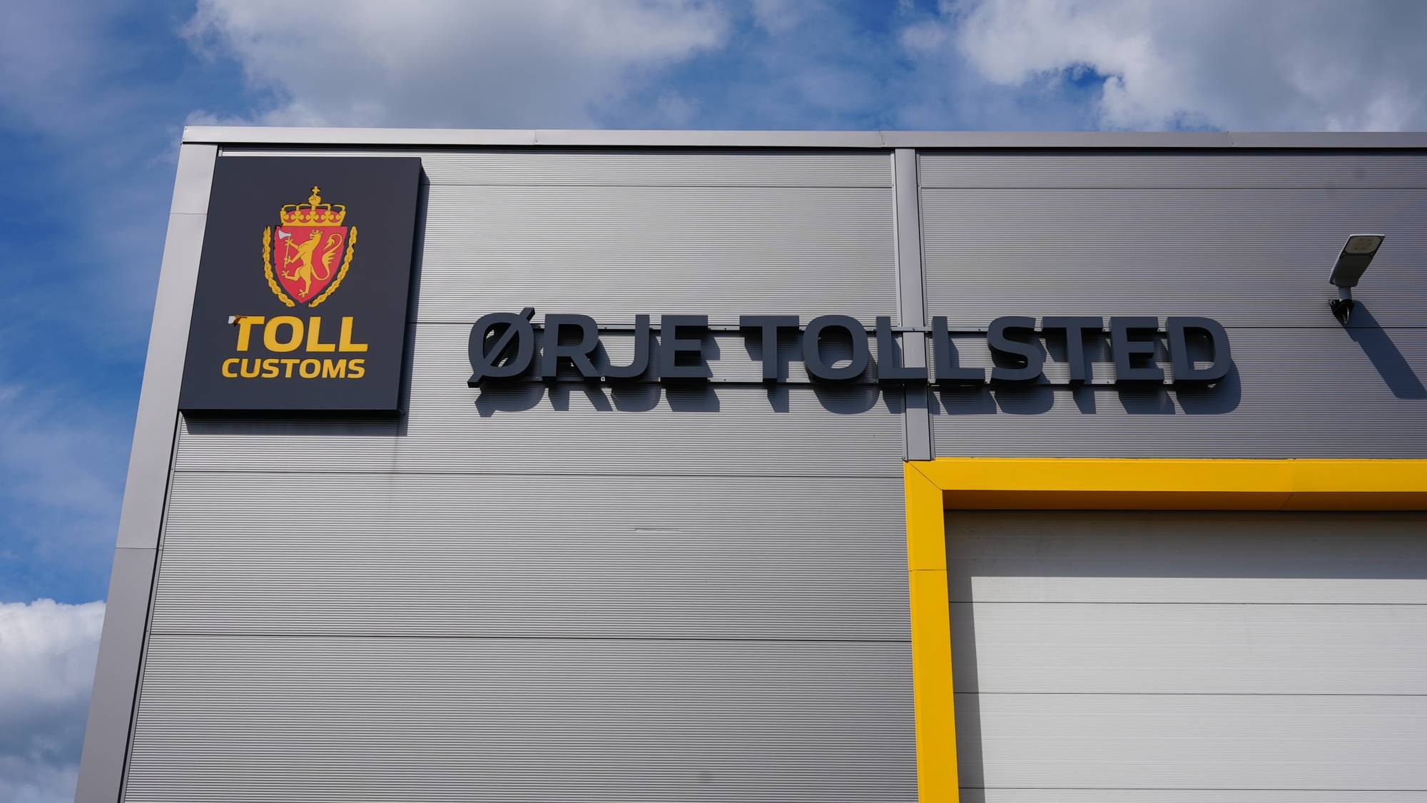Et grått bygg med et skilt hvor det står Ørje Tollsted i store svarte bokstaver.
