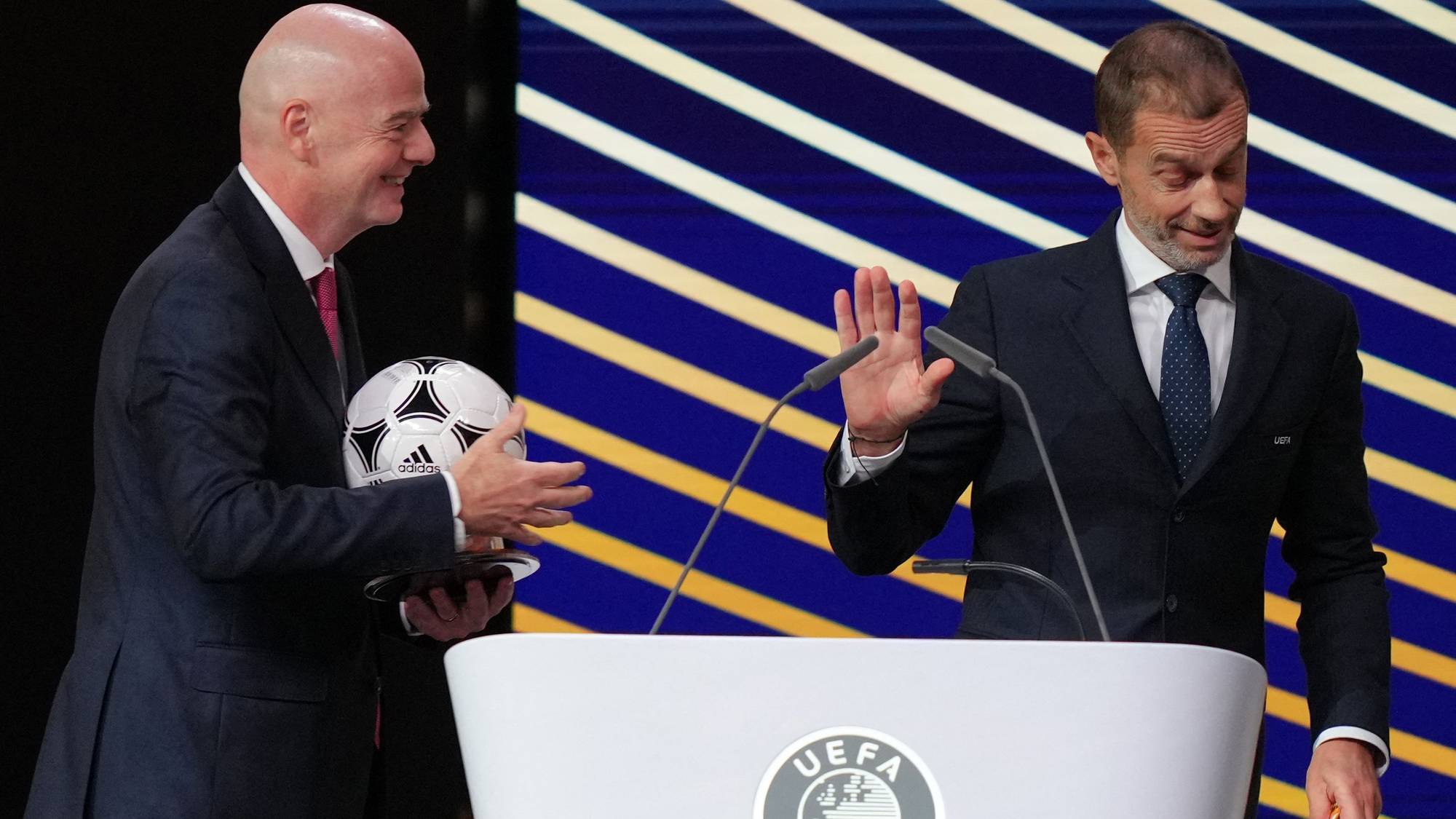 Gianni Infantino og Aleksander Ceferin ved en UEFA-talerstol med en fotball. (Bildebeskrivelsen er laget av en KI-tjeneste)