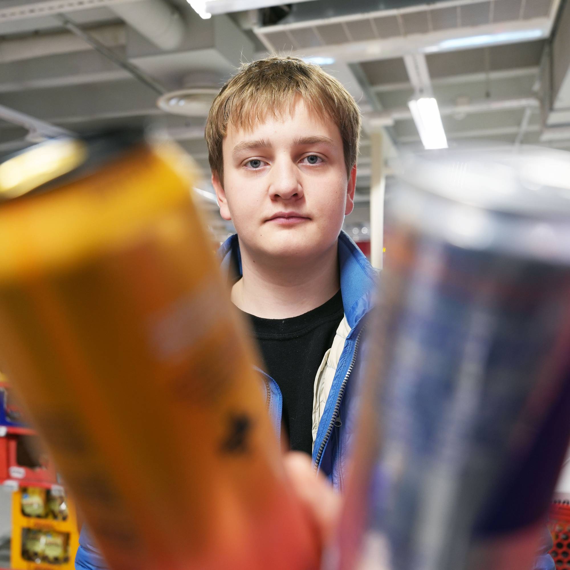 En ung mann står i en dagligvarebutikk og holder to energidrikkbokser foran kameraet. (Bildebeskrivelsen er laget av en KI-tjeneste)