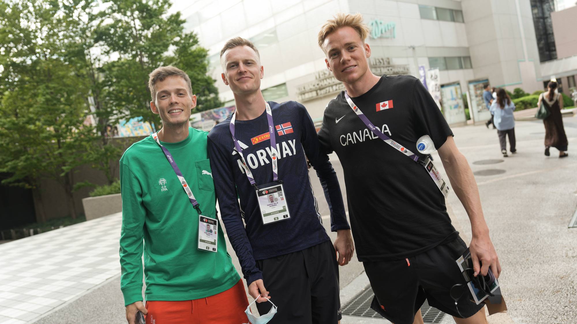 Tre utøvere i sportsklær poserer utendørs foran en bygning. (Bildebeskrivelsen er laget av en KI-tjeneste)