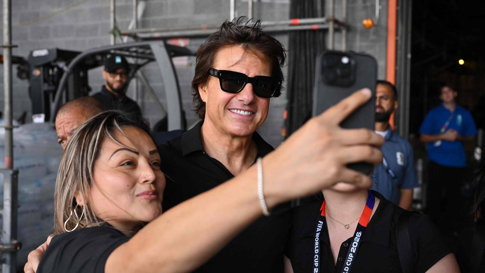 Tom Cruise smiler mens han tar en selfie sammen med en kvinne i et industriområde. (Bildebeskrivelsen er laget av en KI-tjeneste)
