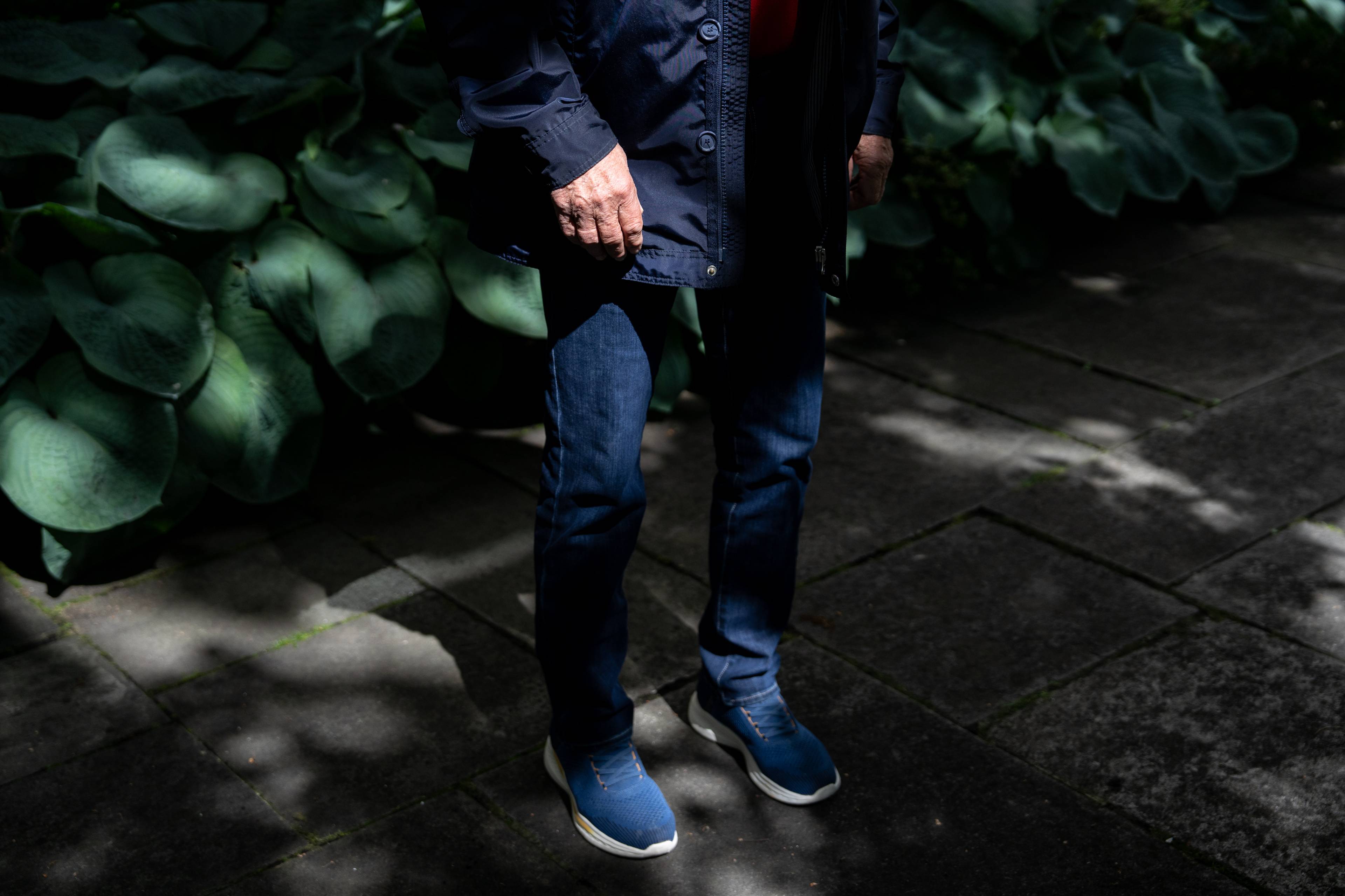 En anonym mann ble blå klær står ute. Han har ryktede hender og står delvis i sol og skygge. Bak ham kan en skimte store blader fra grønne planter.
