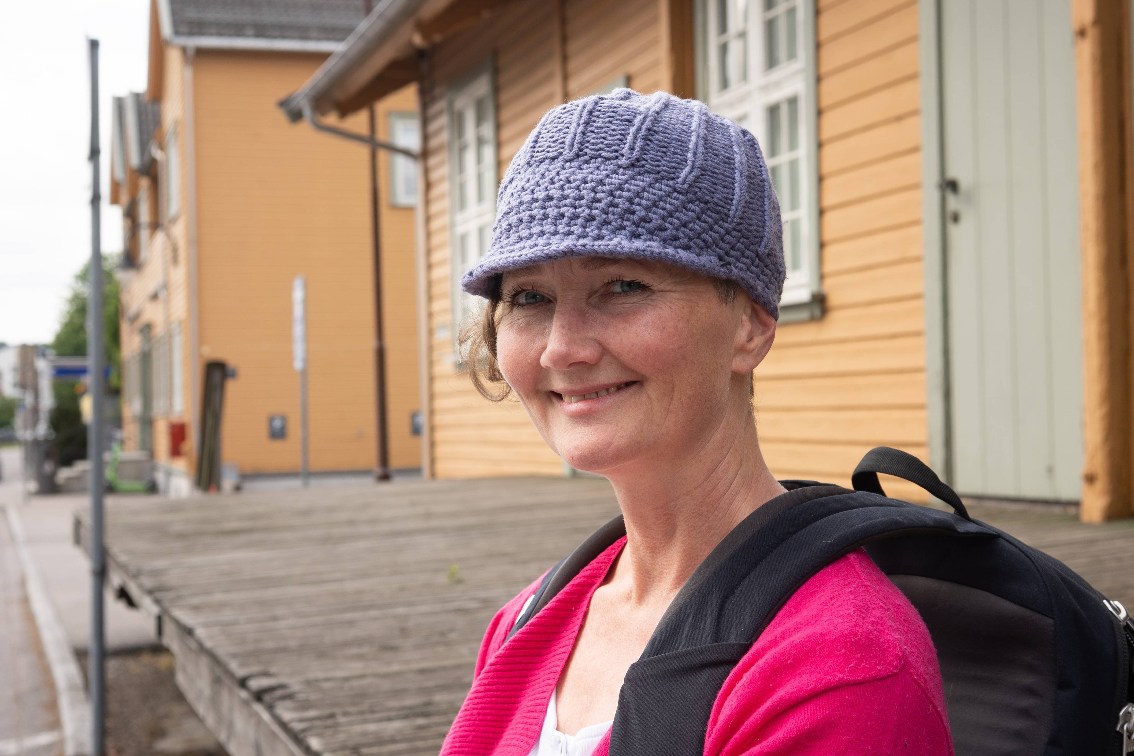 En kvinne smiler mot kameraet iført en strikket lue og rosa genser. Hun har en ryggsekk over skuldrene.