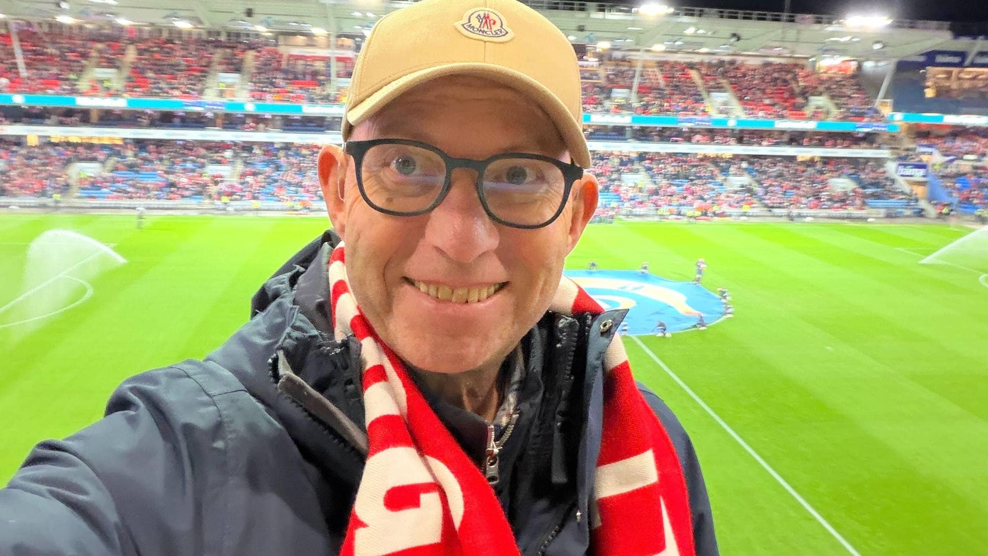 mann med caps og skjerf på en grønn fotballbane 