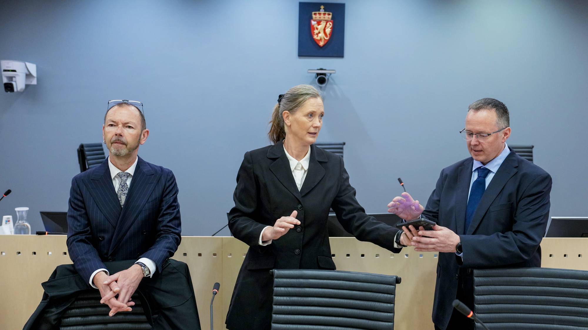 På bildet ser vi tre personer i en rettssal. En kvinne og to menn.