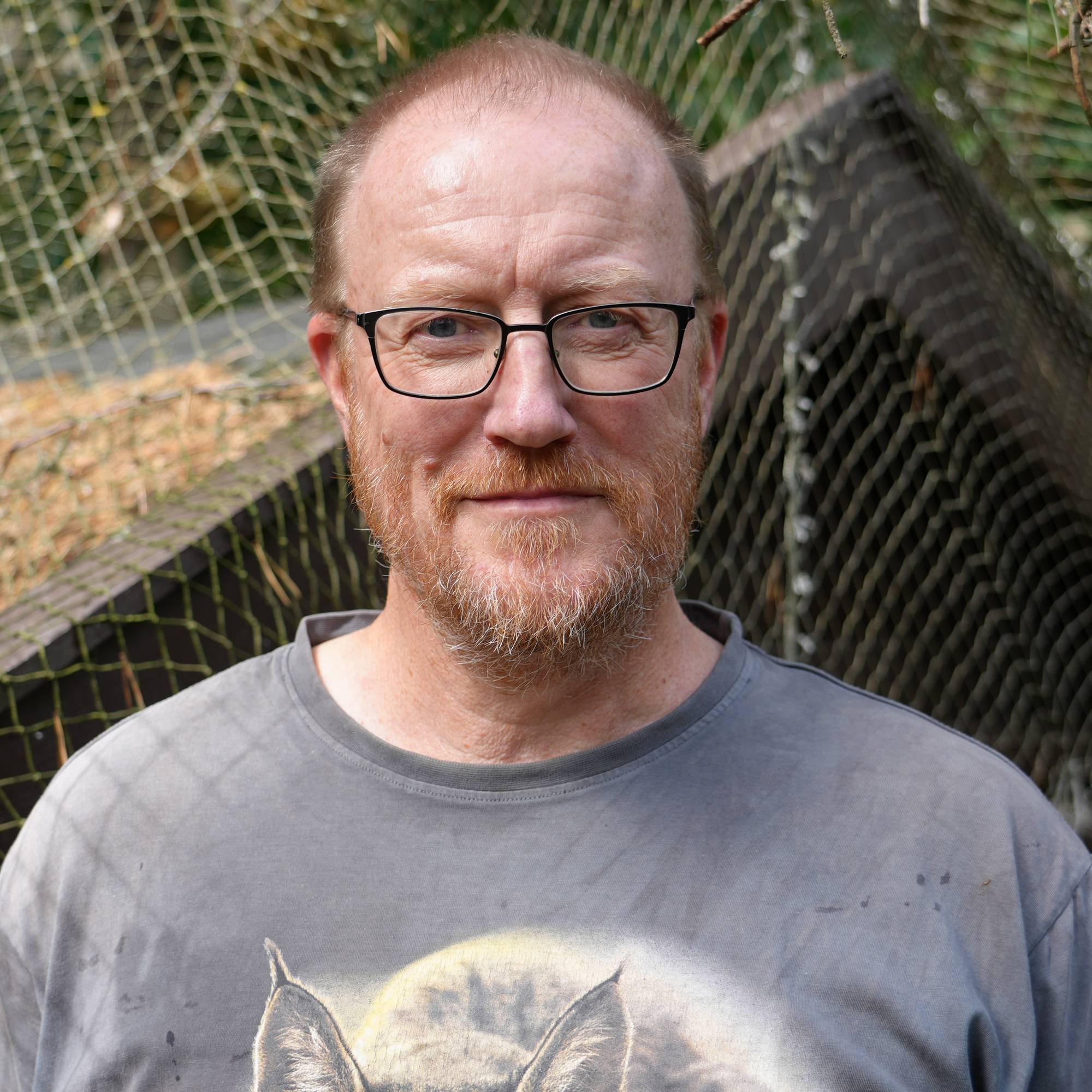 En mann som står foran et hønsehus med netting. I bakgrunnen er det skog.
