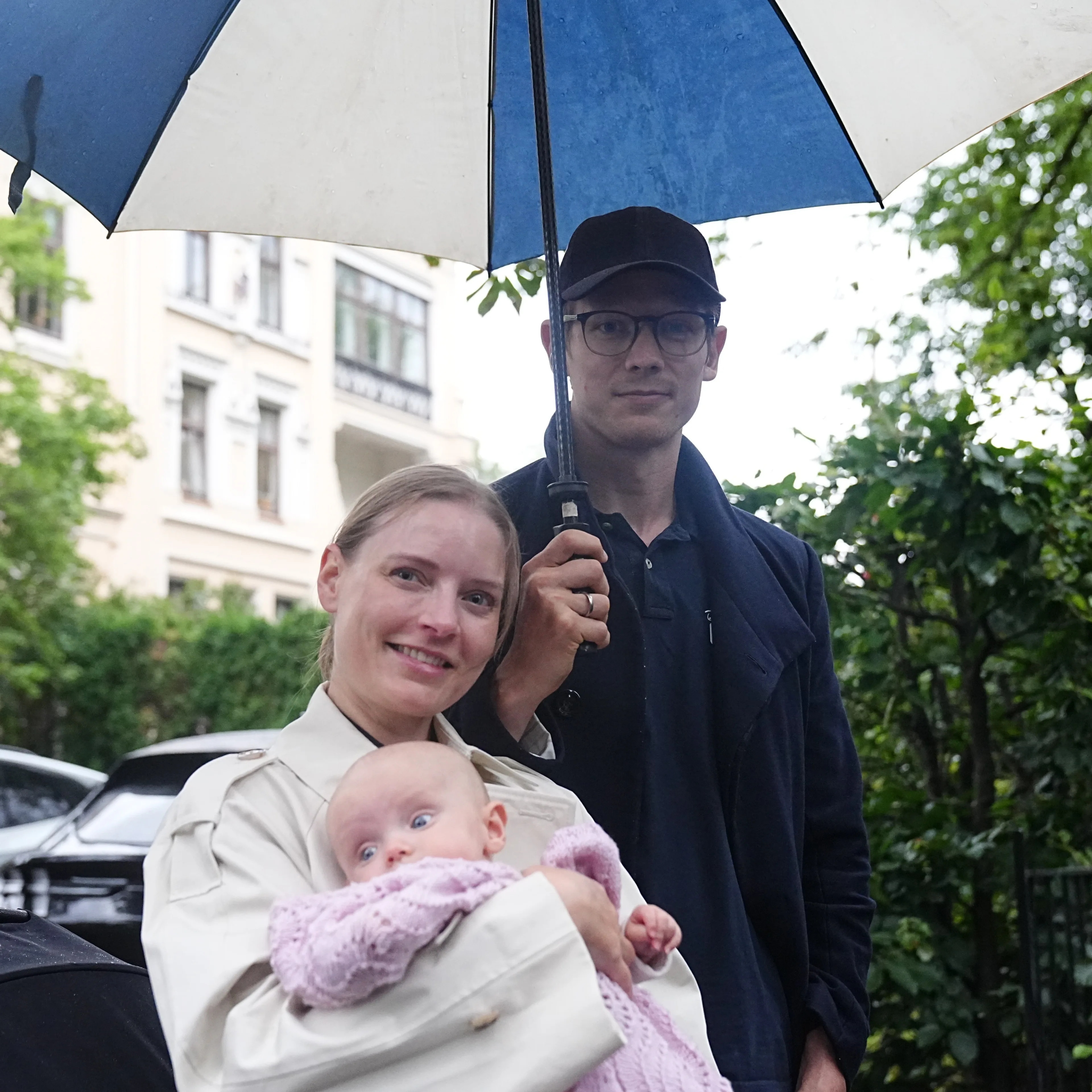 Kvinne og mann med baby under en paraply utendørs. (Bildebeskrivelsen er laget av en KI-tjeneste)
