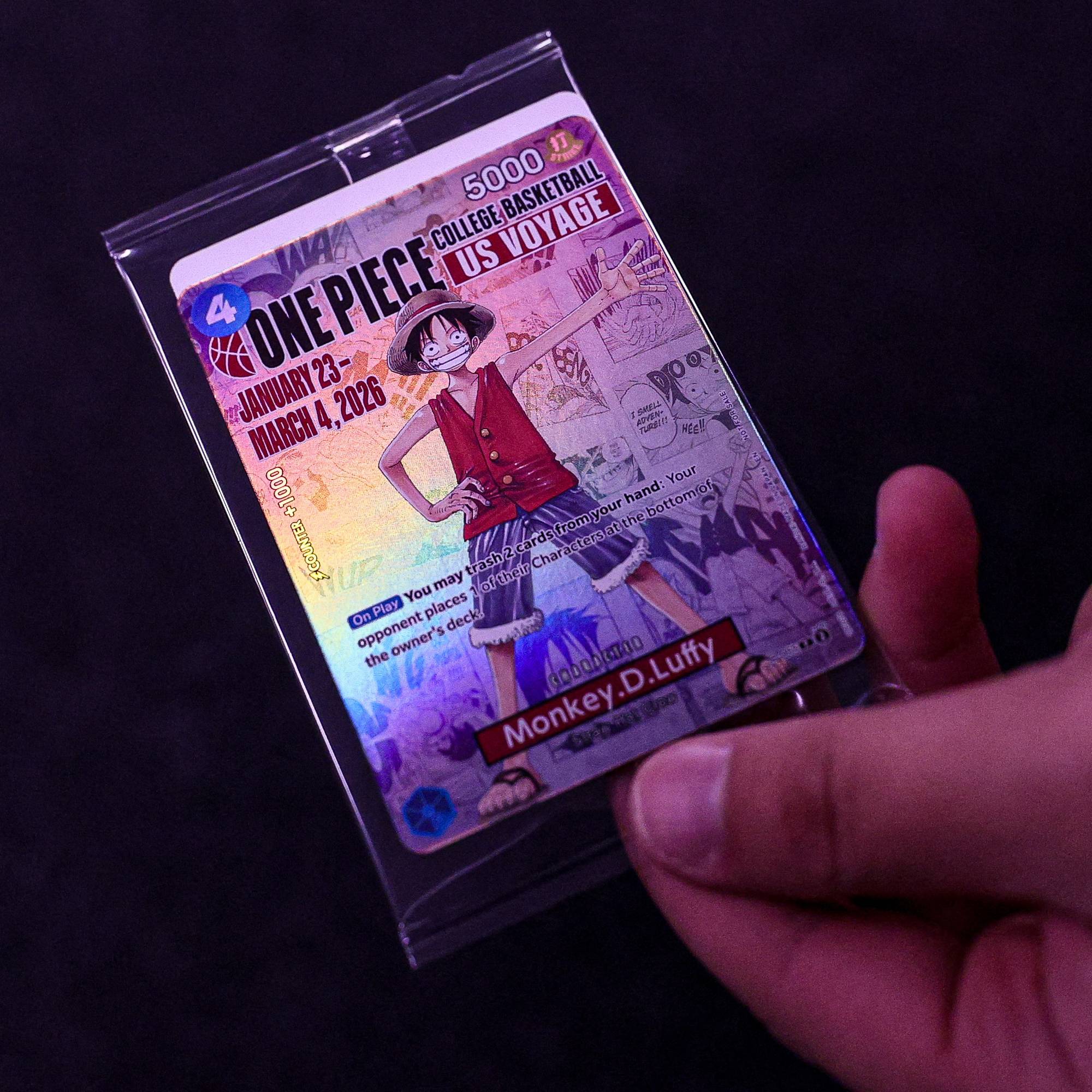 En person holder et spillkort for One Piece US Voyage. Kortet har bilde av Monkey D. Luffy og tekst om datoer og spilleregler. Bakgrunnen er mørk. (Bildebeskrivelsen er laget av en KI-tjeneste)