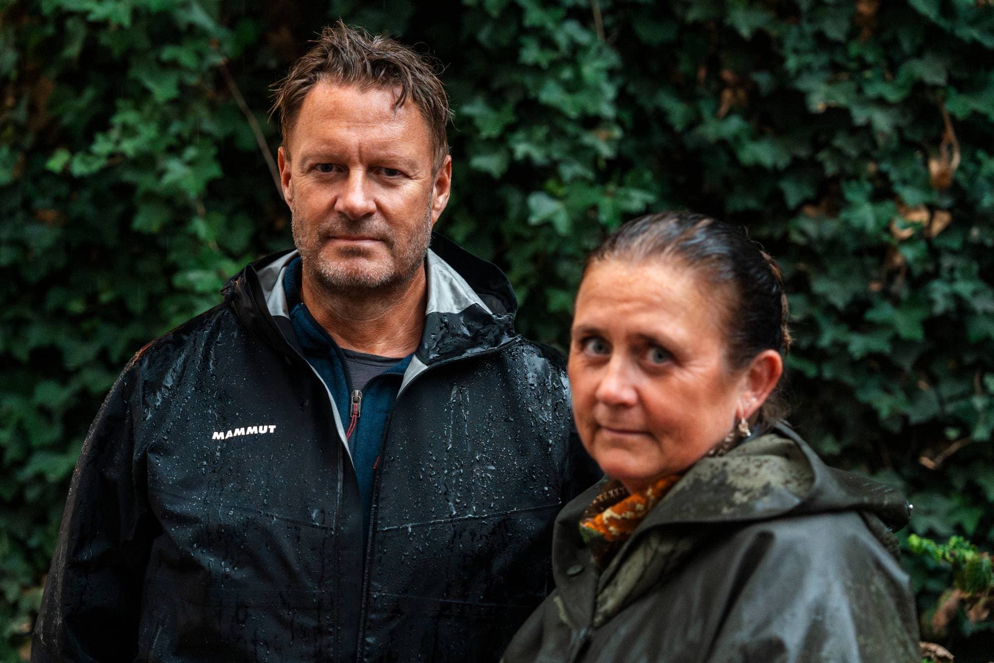 Mann og kvinne i regnklær står foran en grønn vegg av eføy. (Bildebeskrivelsen er laget av en KI-tjeneste)