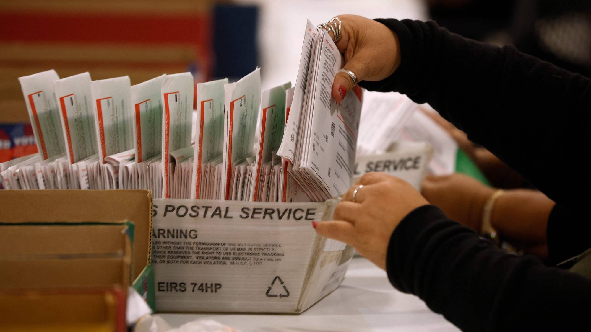 En person sorterer bunker med post i en eske fra US Postal Service. (Bildebeskrivelsen er laget av en KI-tjeneste)