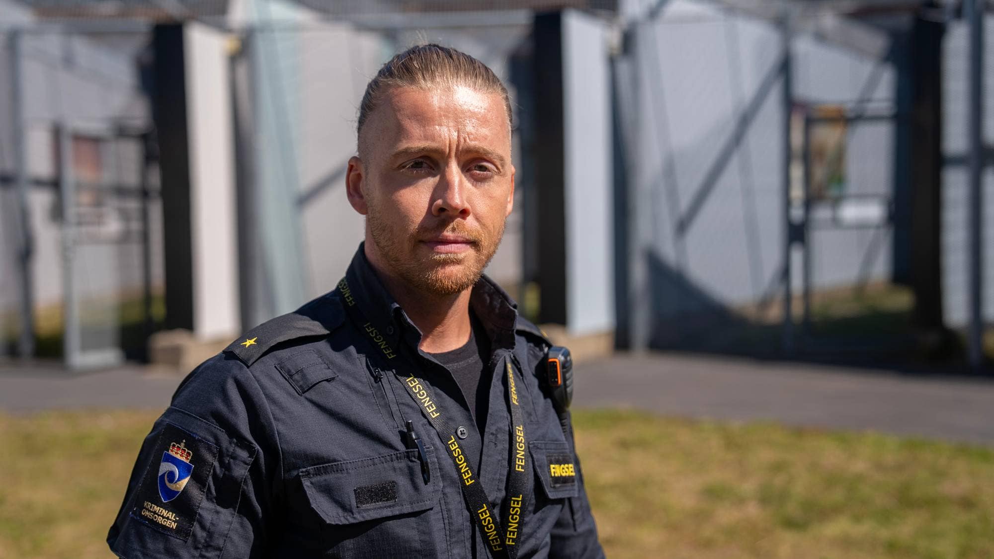 Fengselsbetjent i uniform står foran et fengsel.