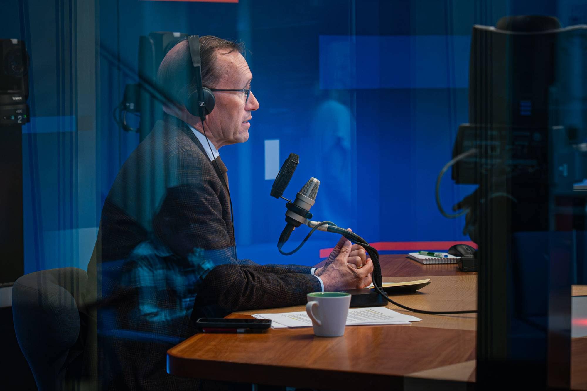 en mann med hodetelefoner og sittende ved et skrivebord med mikrofon (Bildebeskrivelsen er laget av en KI-tjeneste)