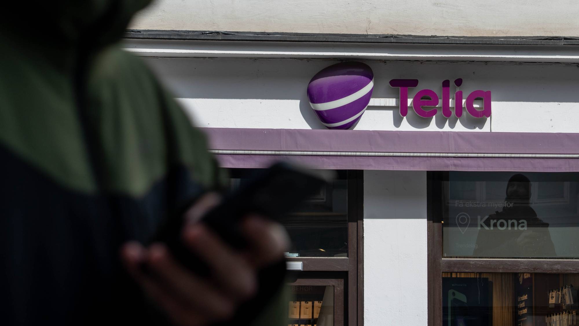 Person med mobil foran Telia-butikk