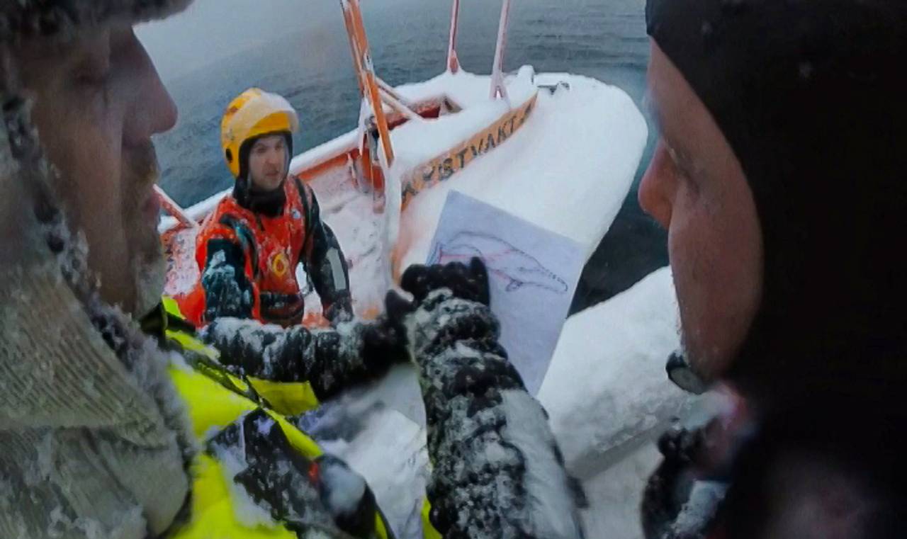 Mannskap fra Tromsø Brann- og redning i båt, ser på tegning av hval som sitter fast