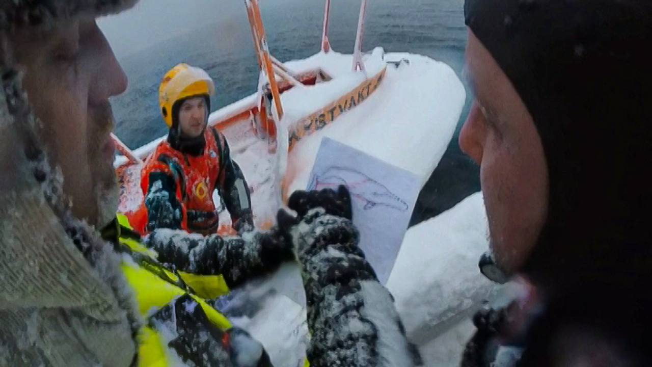 Mannskap fra Tromsø Brann- og redning i båt, ser på tegning av hval som sitter fast