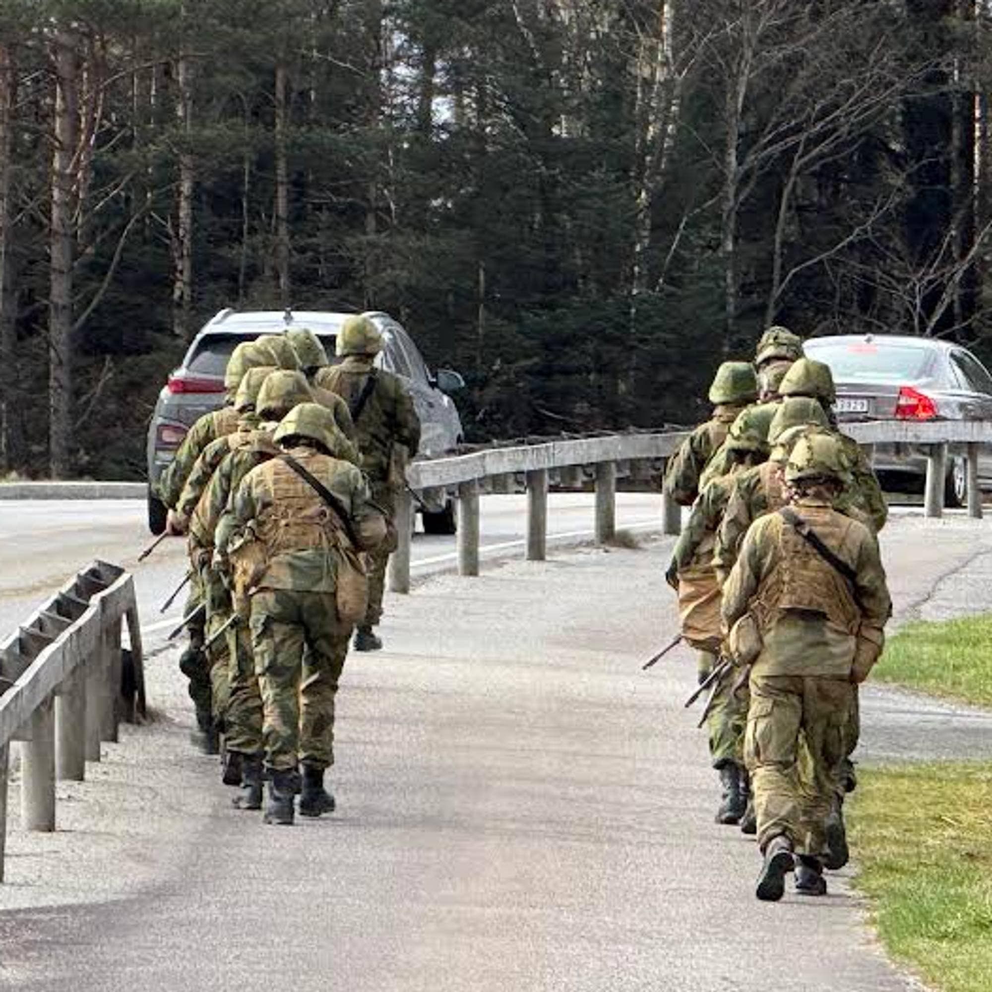 Heimevernøving i Sveio: ca 15 uniformerte soldatar fotograferte bakfrå, marsjerande på to rekker langs ein veg med skog rundt.
