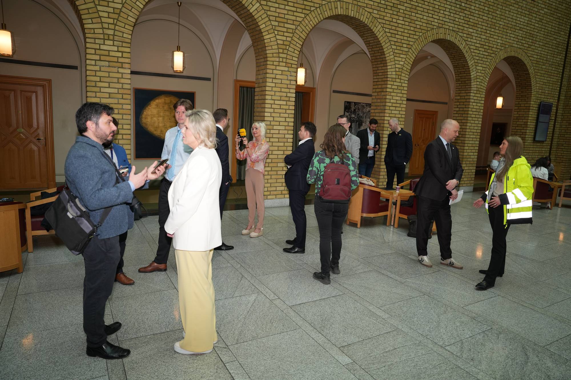 Journalister og politikere på Stortinget. Listhaug og Vedum med hver sin journalist i forgrunnen. Rommet er høyt og i gul murstein.