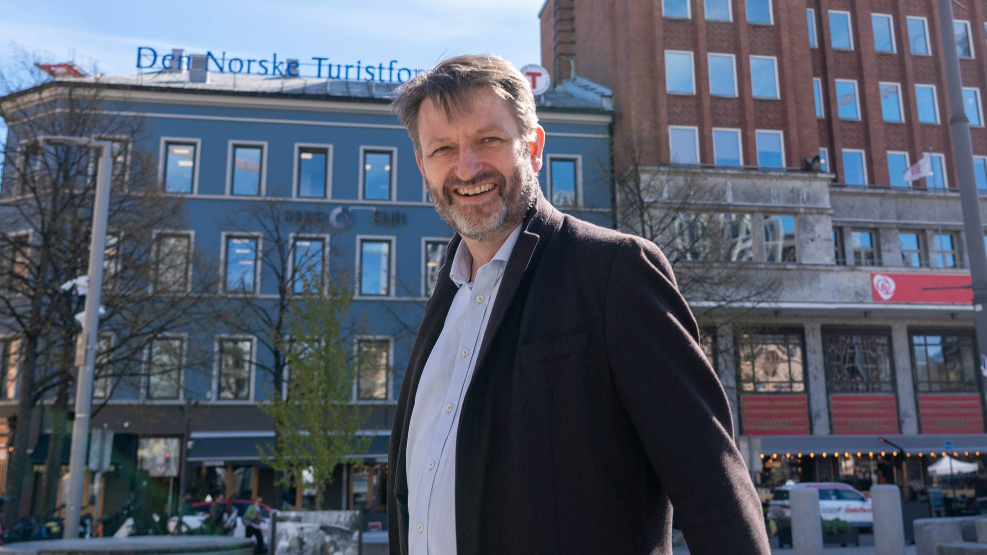 En mann i dress på Youngstorget i Oslo. Han smiler bredt og har ansiktet vendt mot kameraet. 