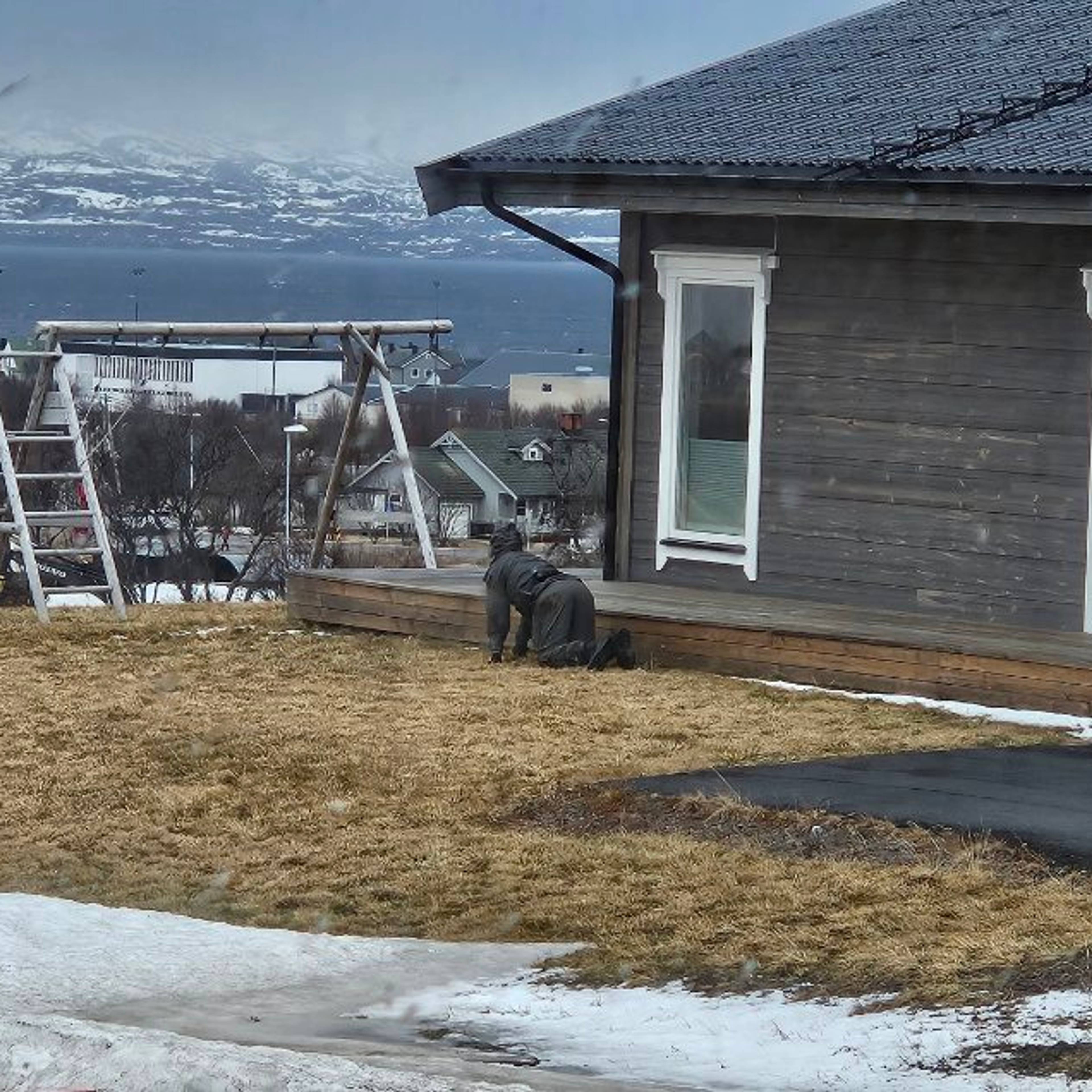 En ansatt i politiet kryper langs en husvegg ikledd mørke klær.