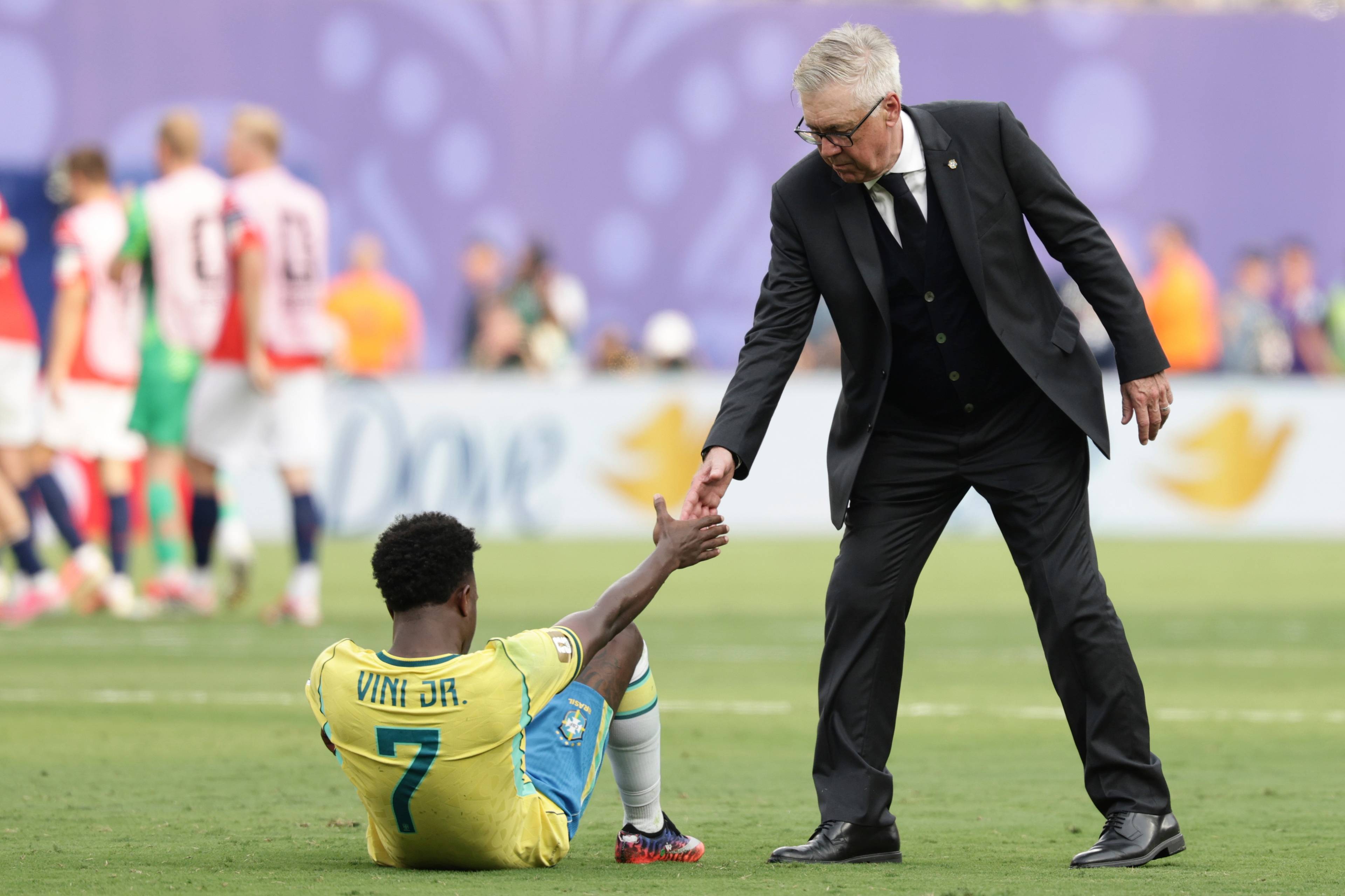 Carlo Ancelotti hjelper Vincius Jnior opp fra gresset under en fotballkamp. (Bildebeskrivelsen er laget av en KI-tjeneste)