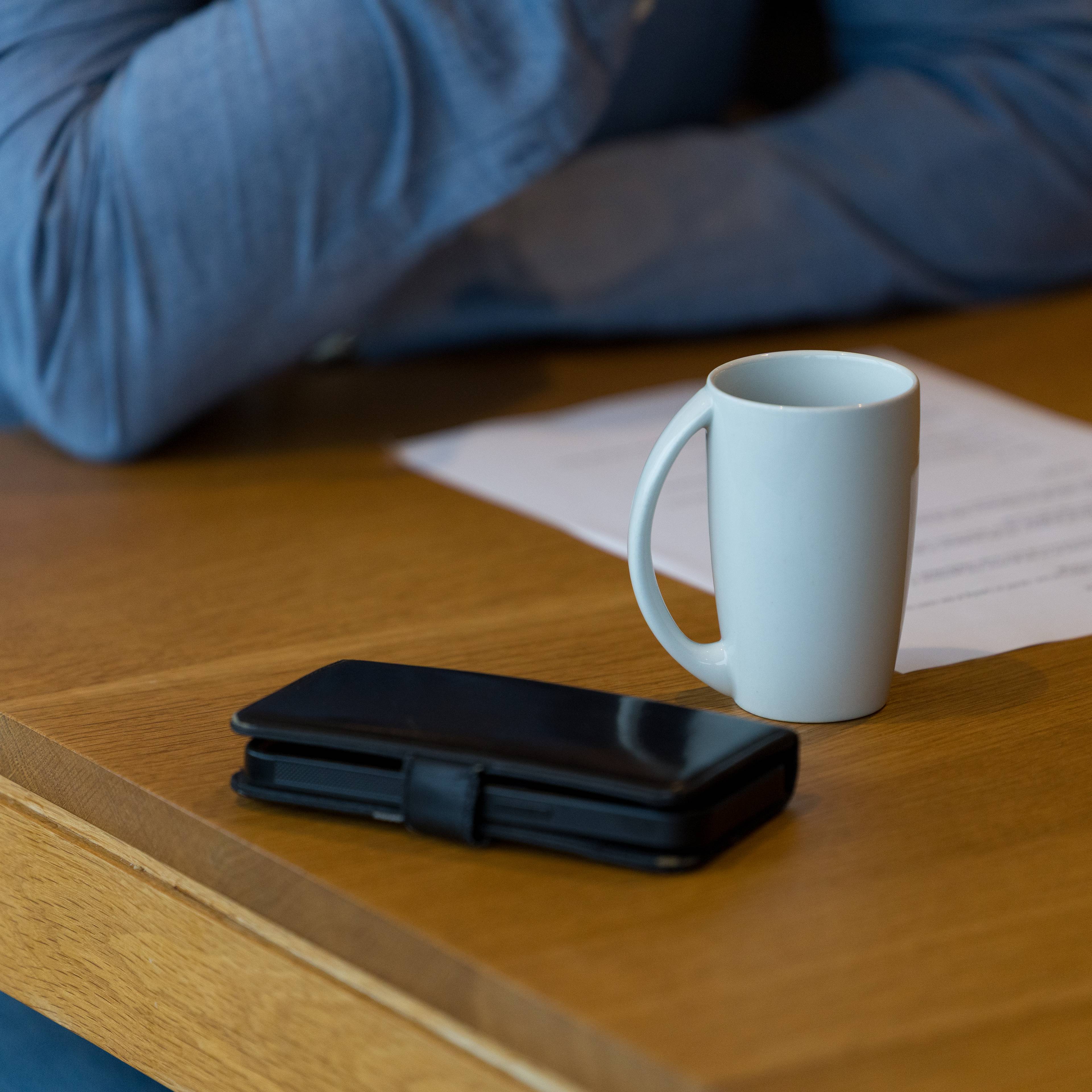Erik Bjerkaas lener seg på bordet. Du ser kun armene, og bildet fokuserer på en hvit kaffekopp og mobilen som ligger der.